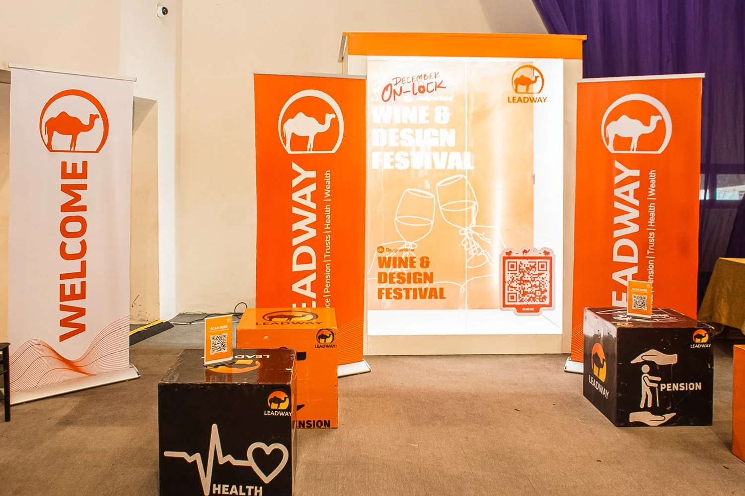 Event display for the Wine & Design Festival with four vertical banners, two black cubes, and an orange box, all branded with Leadway, featuring wine glass illustrations, QR codes, and text promoting health, pension, and pension-related services at t