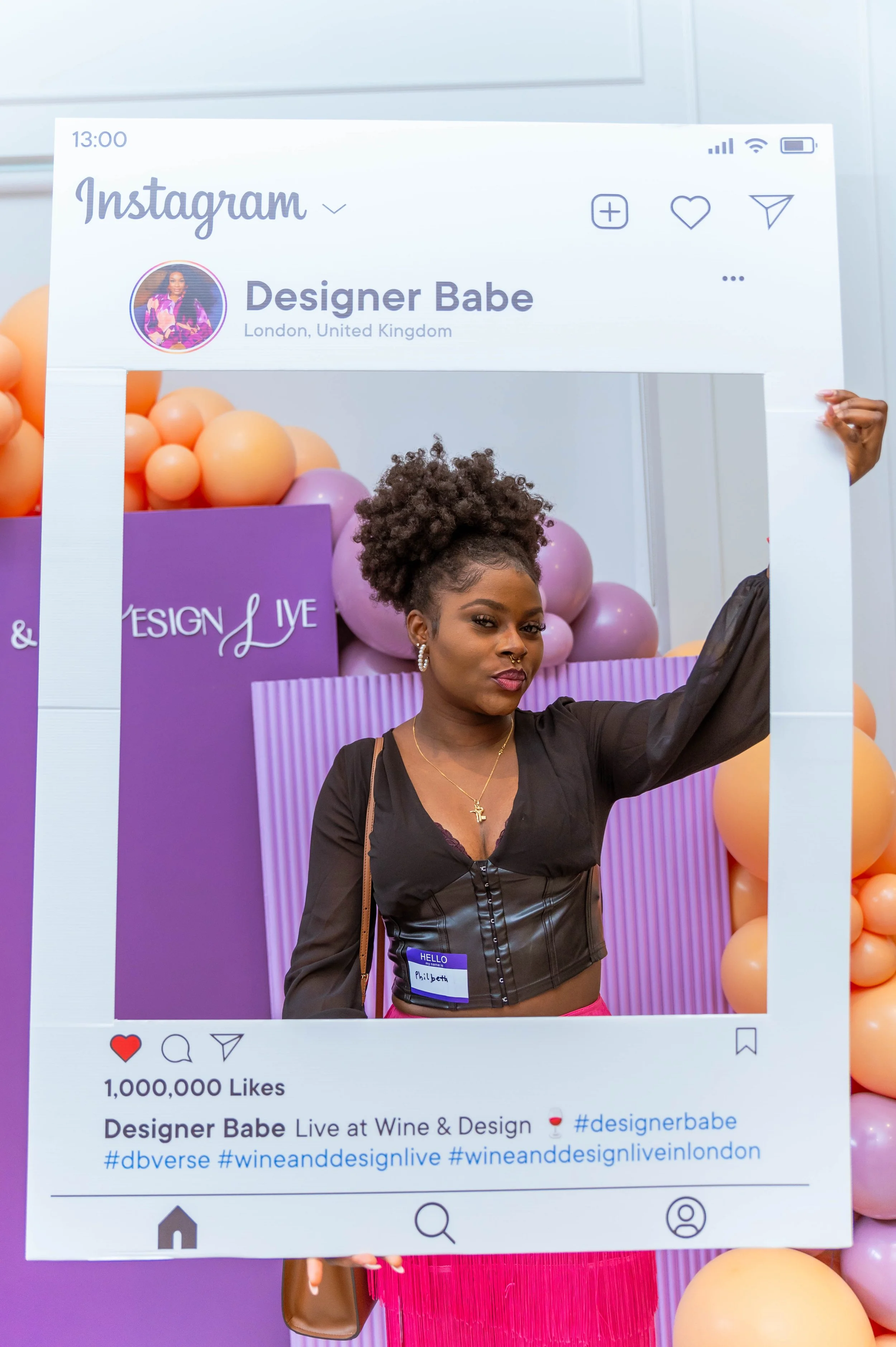 A woman holding a large Instagram photo frame at an event, with colorful balloons and a purple backdrop in the background.