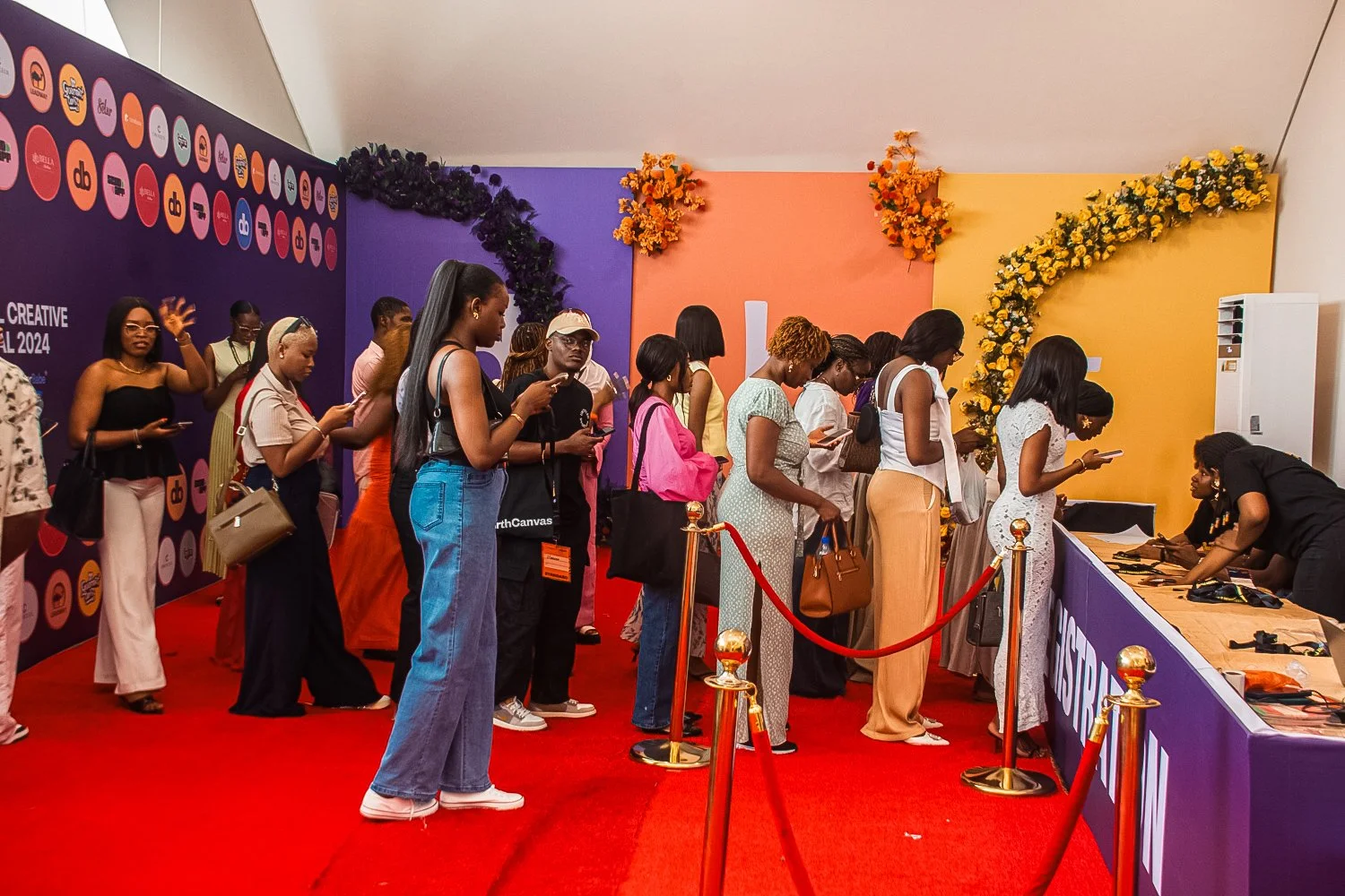People standing in line at an event registration booth with purple and yellow decorated walls and floral arrangements.