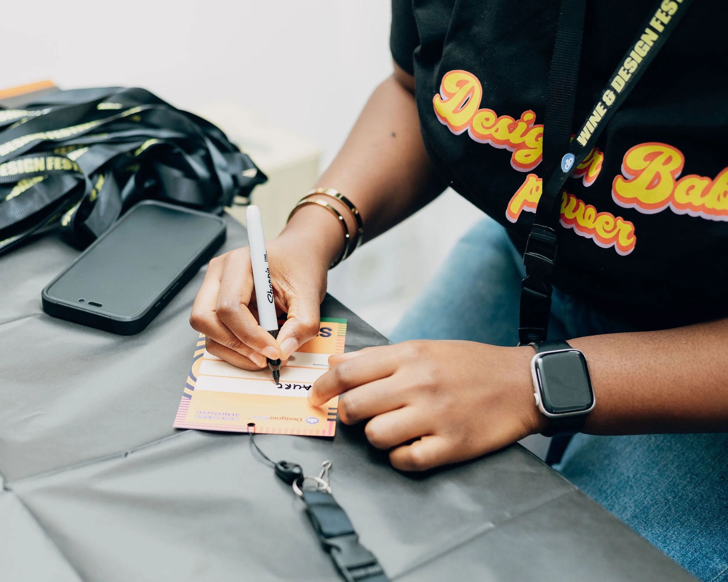 Person signing a boarding pass at a table with a smartphone, luggage, and a smartwatch on their wrist.