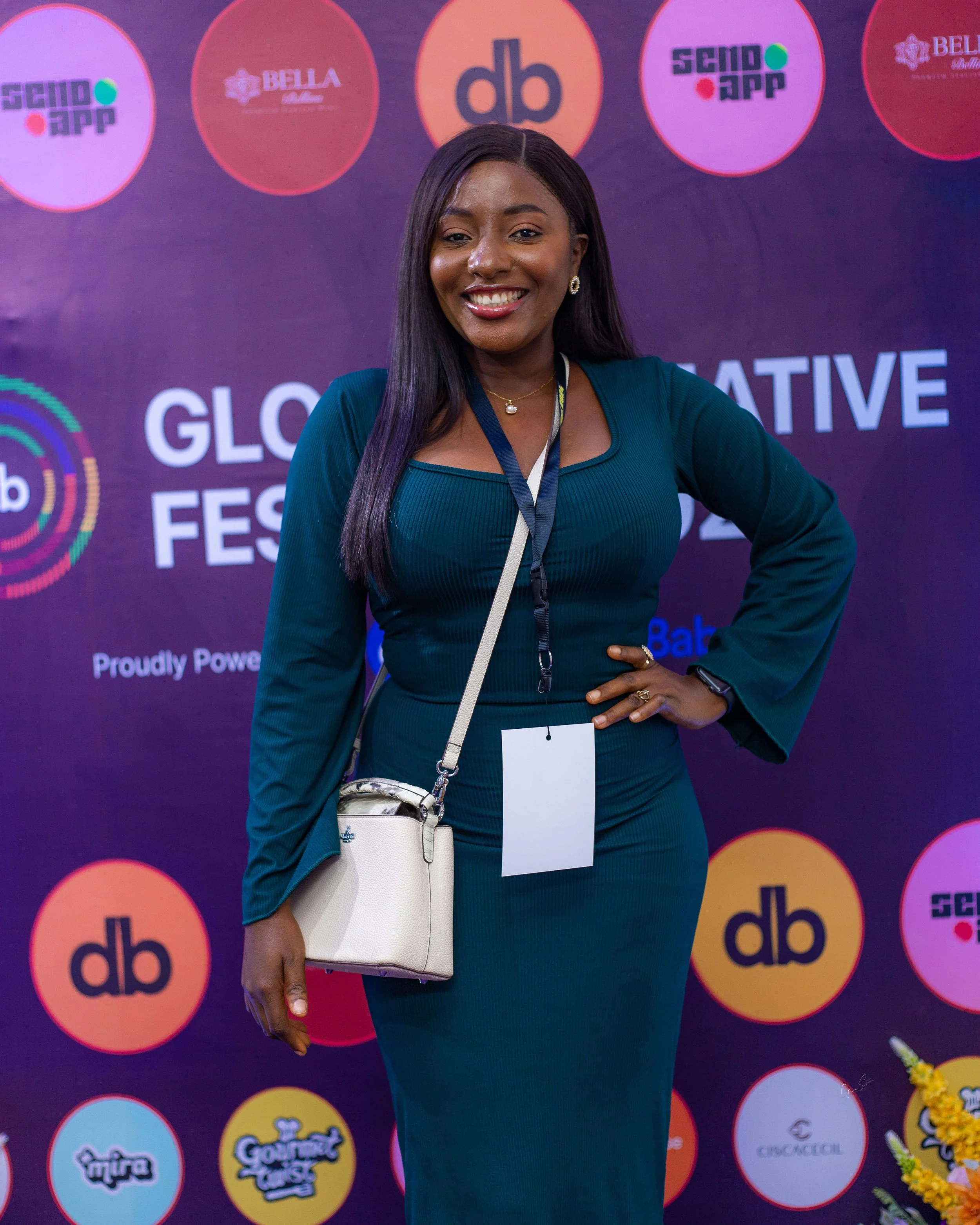 A woman smiling at a gender reveal festival event, standing in front of a colorful backdrop with logos and text.