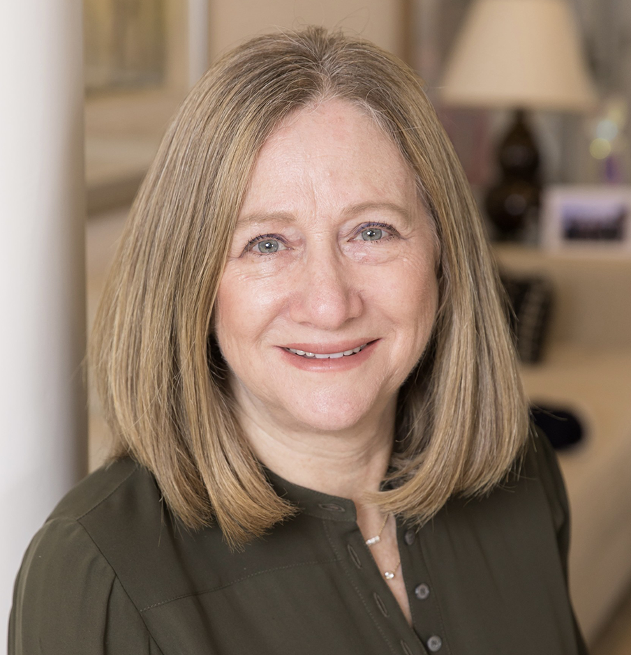Recognizing Martine Fleishman, smiling, wearing a forest green blouse, in her home.