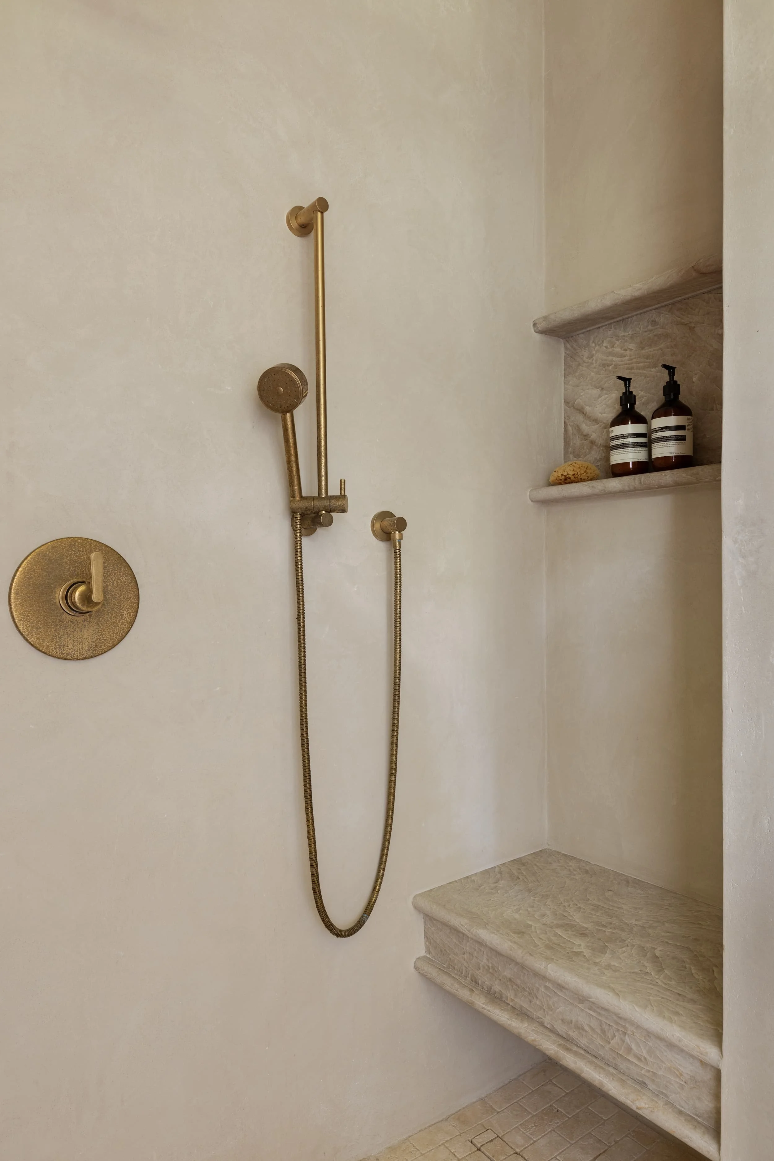 A spa-like walk-in shower in the Chicago primary suite renovation features tadelakt plaster walls, a marble bench, and brass fixtures, blending modern luxury with timeless materials.
