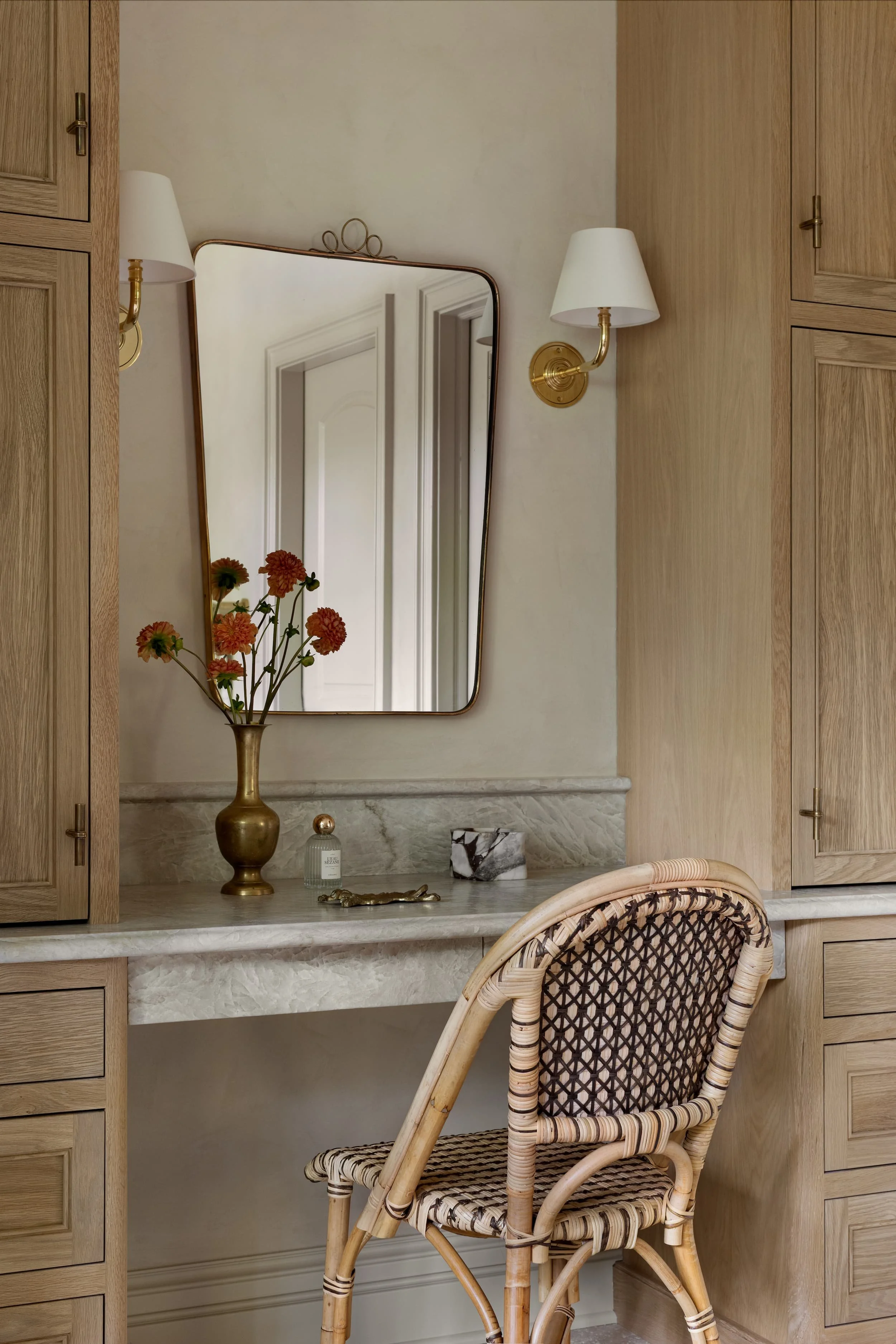 A chic makeup vanity in the Chicago primary suite renovation combines taj mahal stone, brass accents, and a vintage rattan chair, reflecting Studio Burgoon’s layered and intentional design approach.