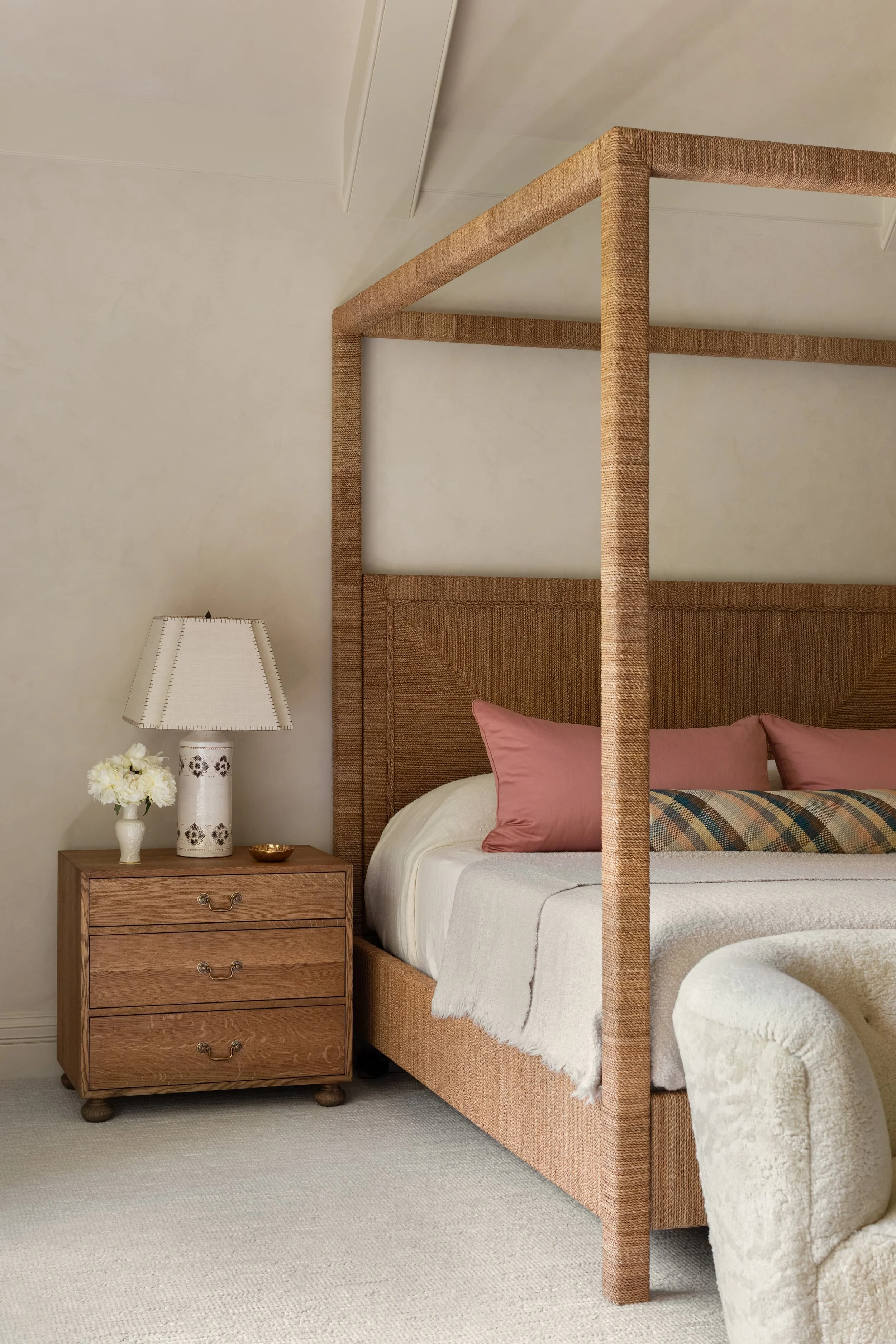 Chicago primary suite featuring a woven canopy bed, oak nightstands, and layered bedding in warm neutrals with soft pink and plaid woven leather accents.