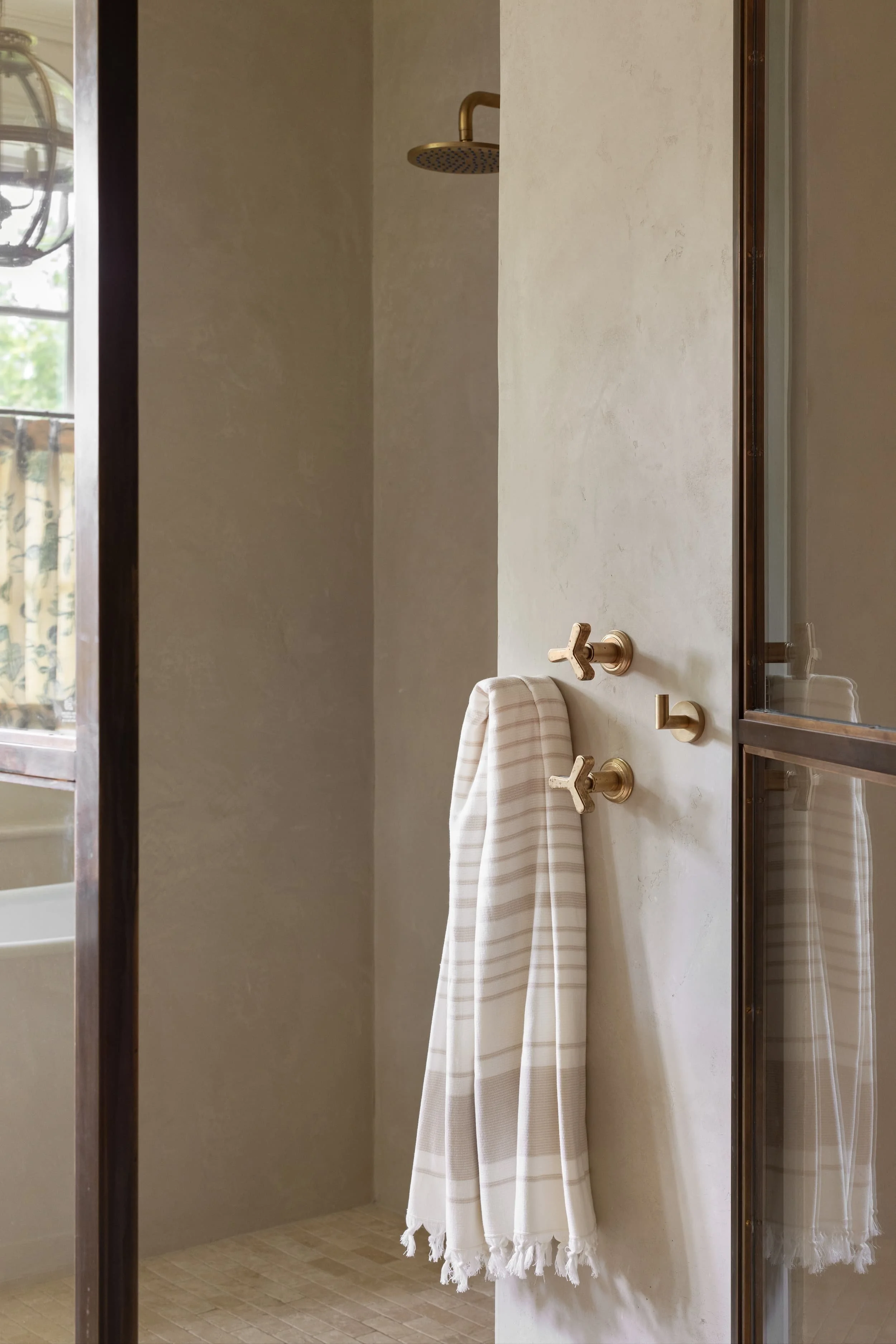 Chicago primary suite bathroom with brass-and-glass shower enclosure, tadelakt plaster walls, and timeless brass fixtures for a modern classic look.