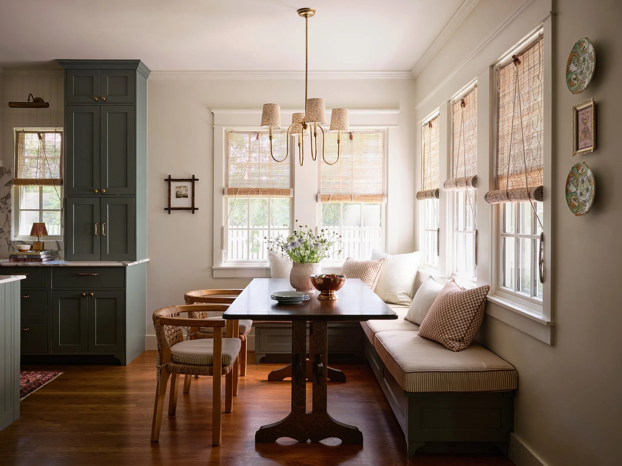Bright kitchen with large windows, green cabinetry, a dining table with four chairs, and a cozy built-in bench with cushions.