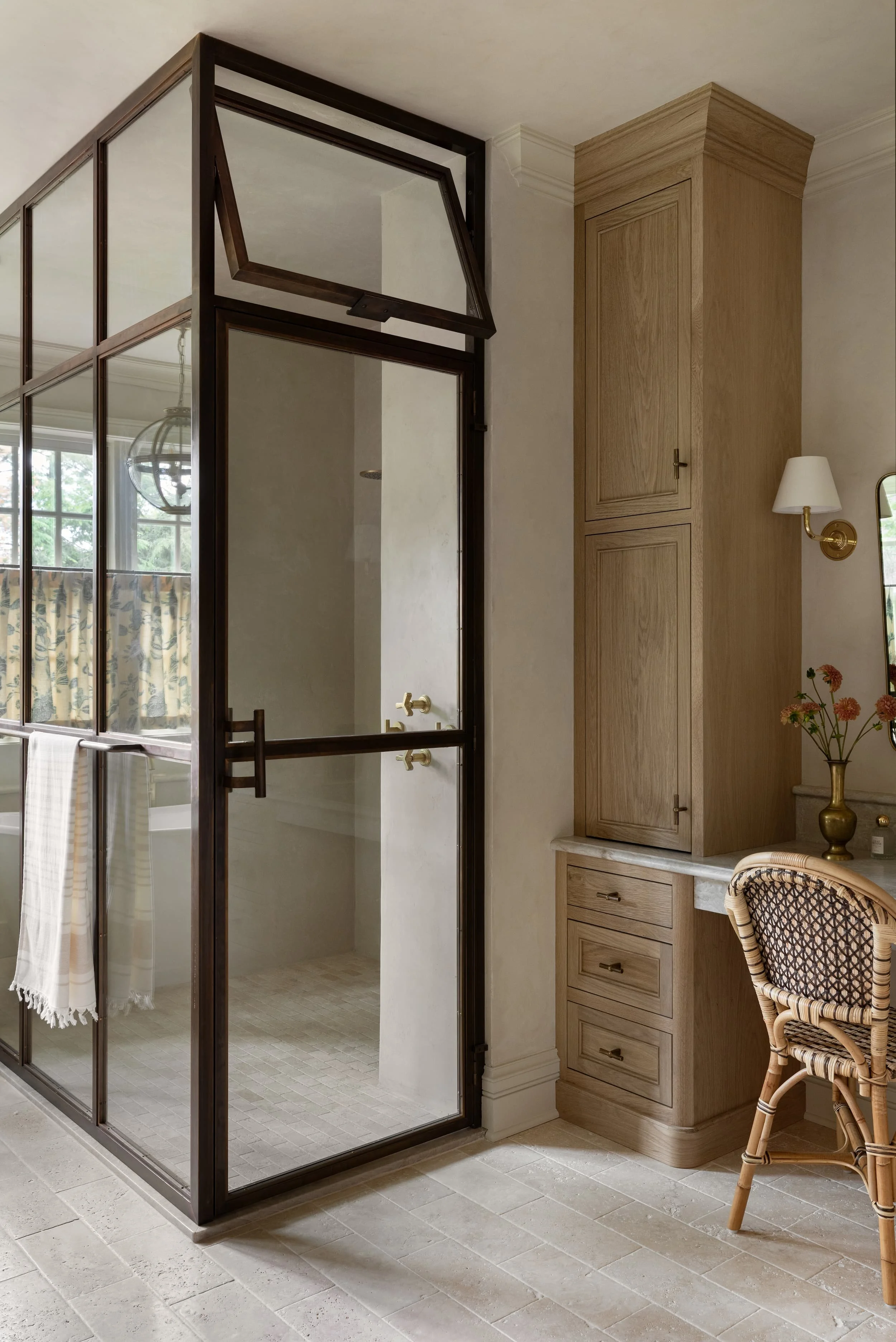 A custom burnished brass and glass shower enclosure with operable transom window anchors the Chicago primary suite renovation, balancing historic charm with modern craftsmanship by Studio Burgoon.