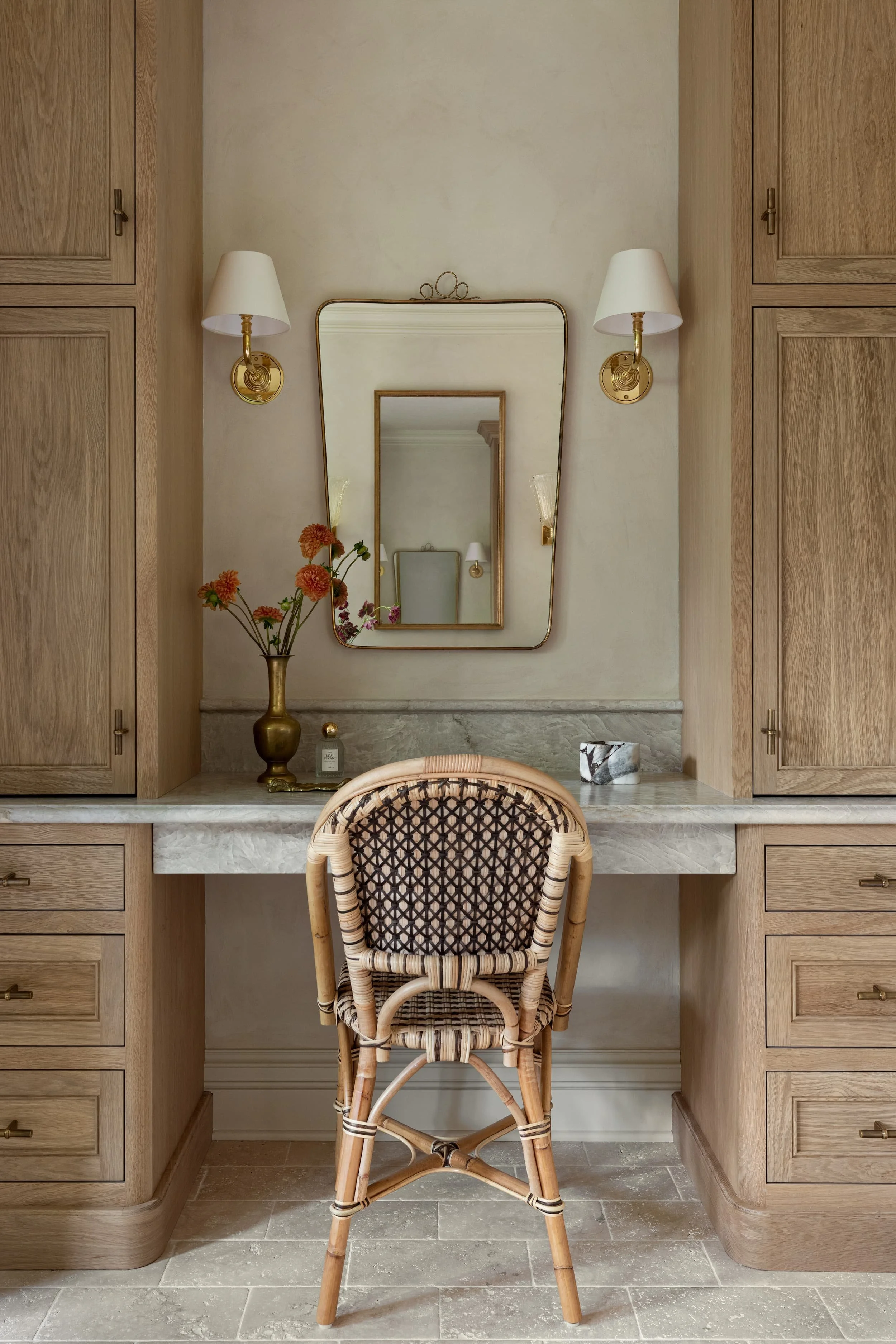 This custom built-in make-up vanity wall with flanking oak cabinetry, leathered taj mahal quartzite top, vintage Italian mirror, and brass sconces provides elegant functionality within the Chicago primary bathroom renovation.
