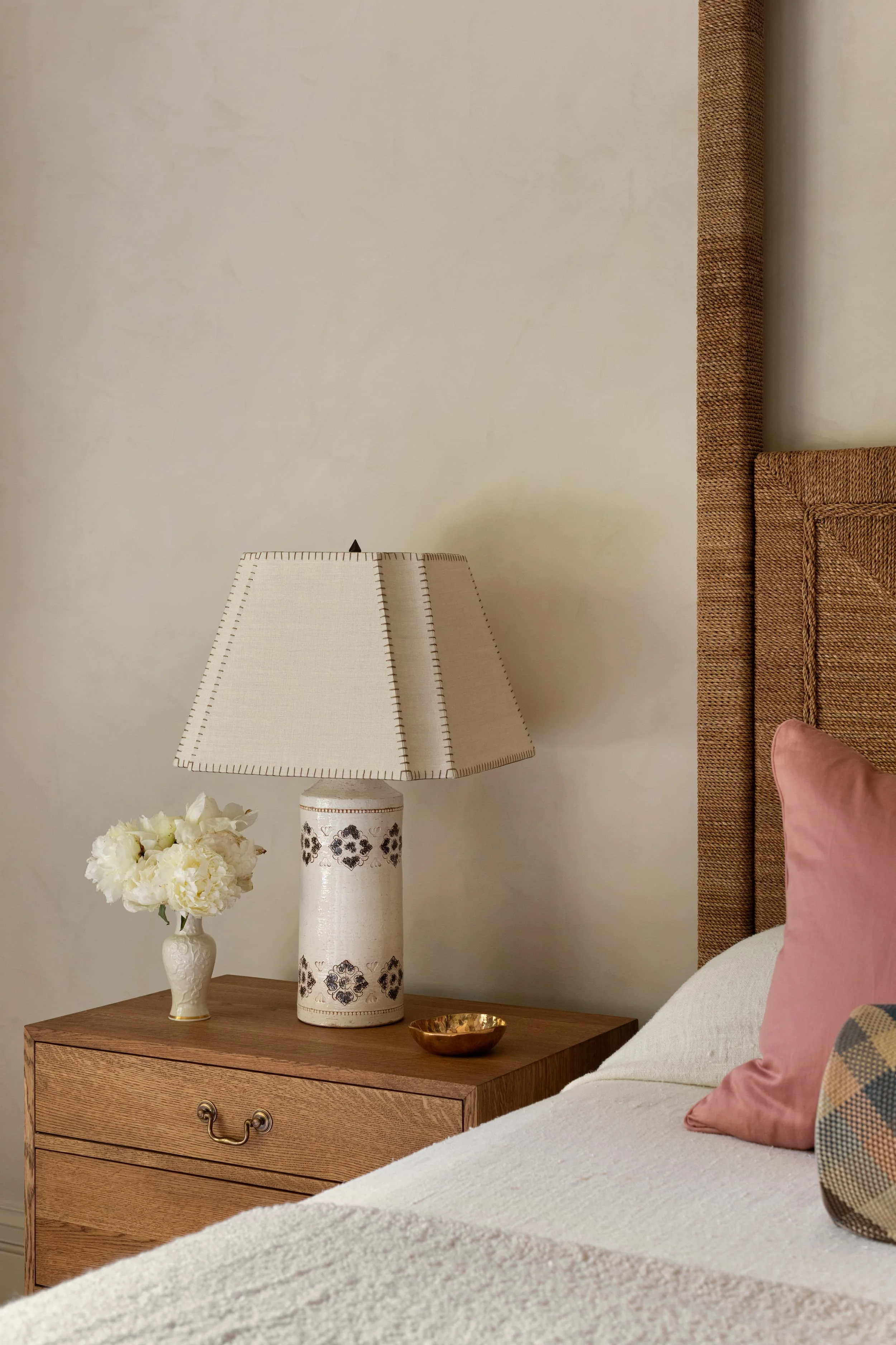 Bedside detail in Chicago primary suite renovation with vintage ceramic lamp, oak nightstand, and layered textural accents.