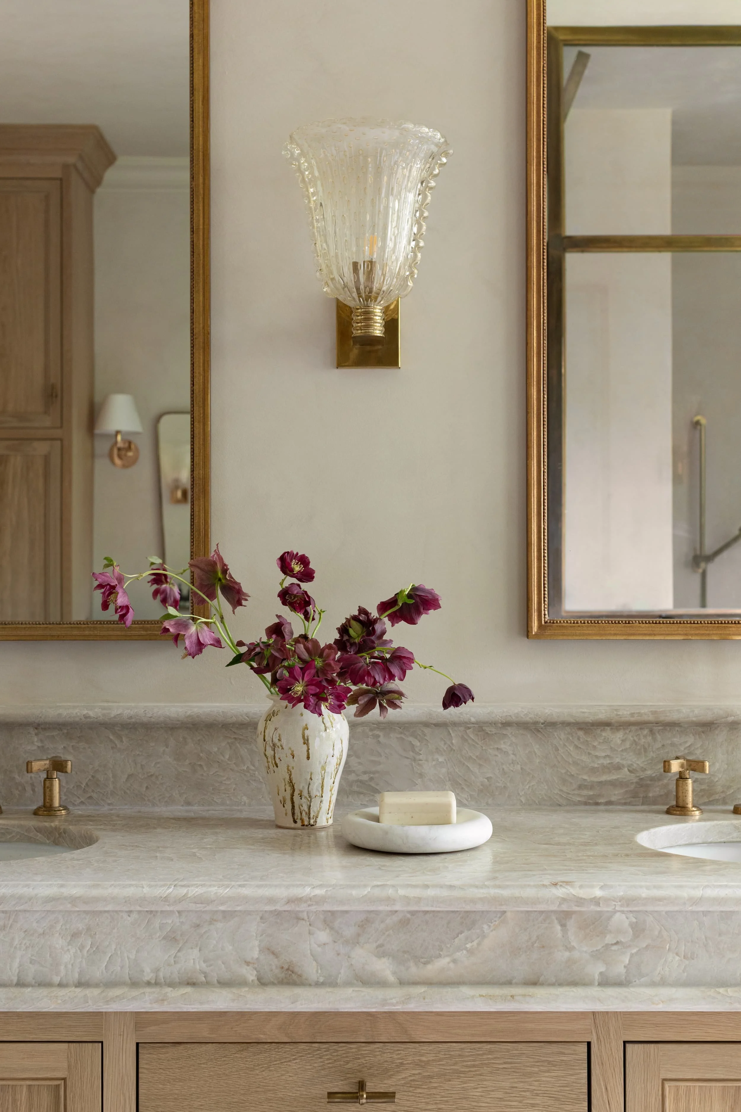 Detail of the marble vanity in the Chicago primary bathroom renovation, featuring brass fixtures, vintage Murano glass sconces, and fresh floral styling for an elevated, artisanal touch.