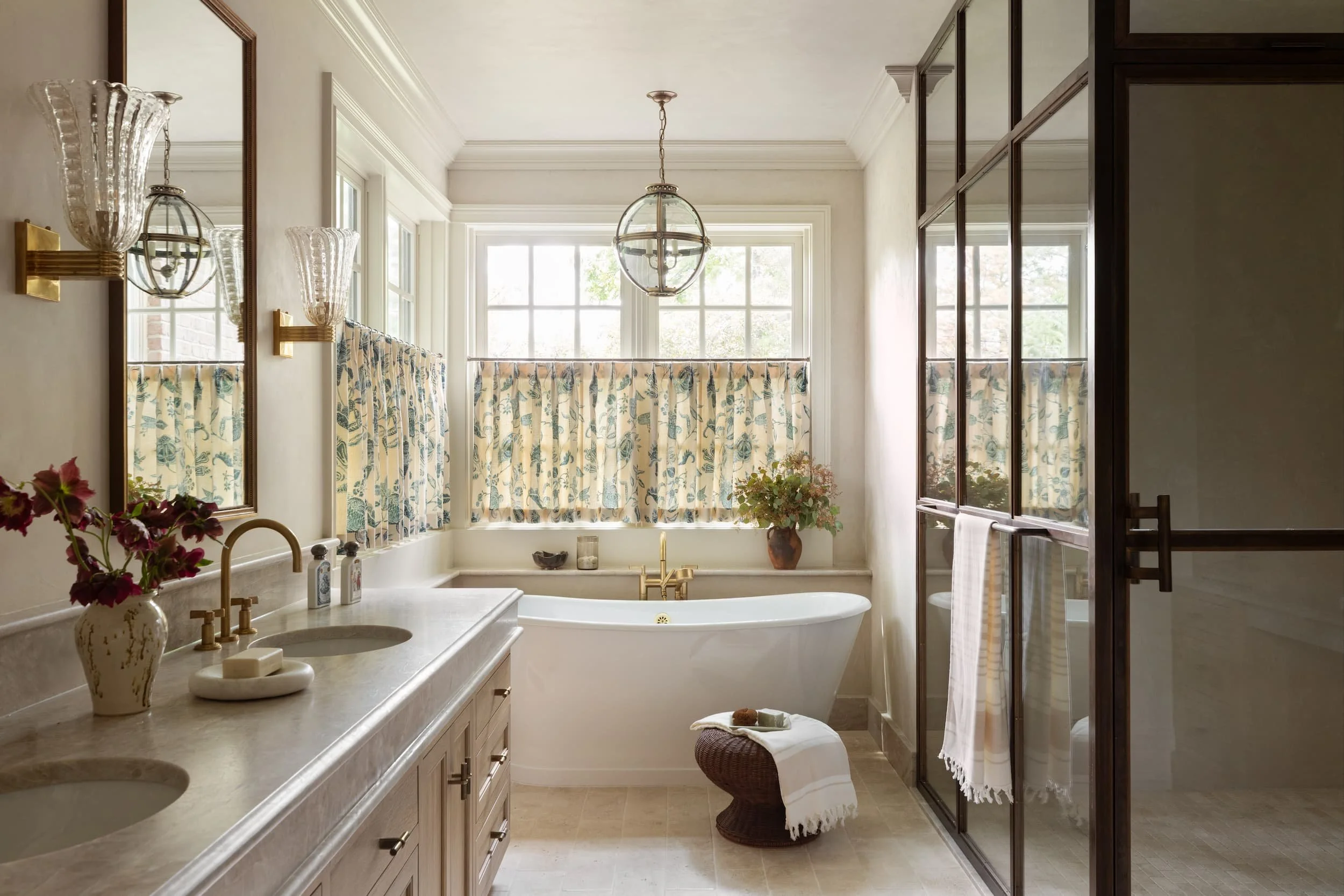 Chicago primary suite bathroom with marble double vanity, freestanding tub, floral café curtains, and brass fixtures by Studio Burgoon.