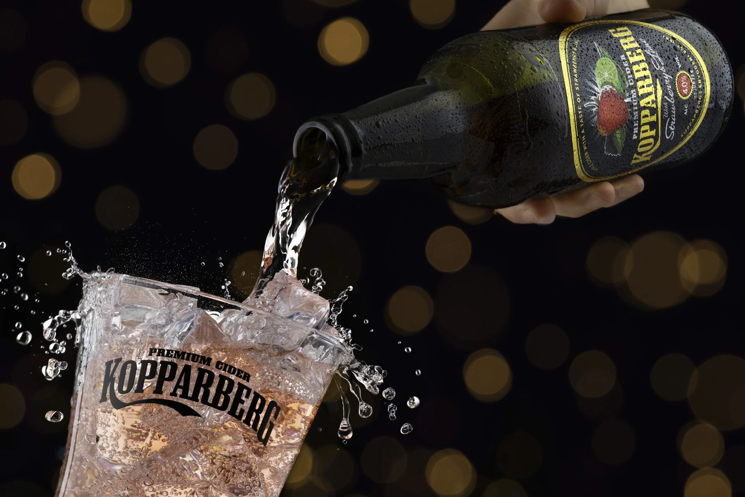 Kopparberg image by Emily Mills, commercial photographer. Created at Emily Mills photographic studio, Devon. Bottle pouring into Kopparberg glass with splashes and bokeh in the background https://www.emilymillsphotography.com/foodanddrink
