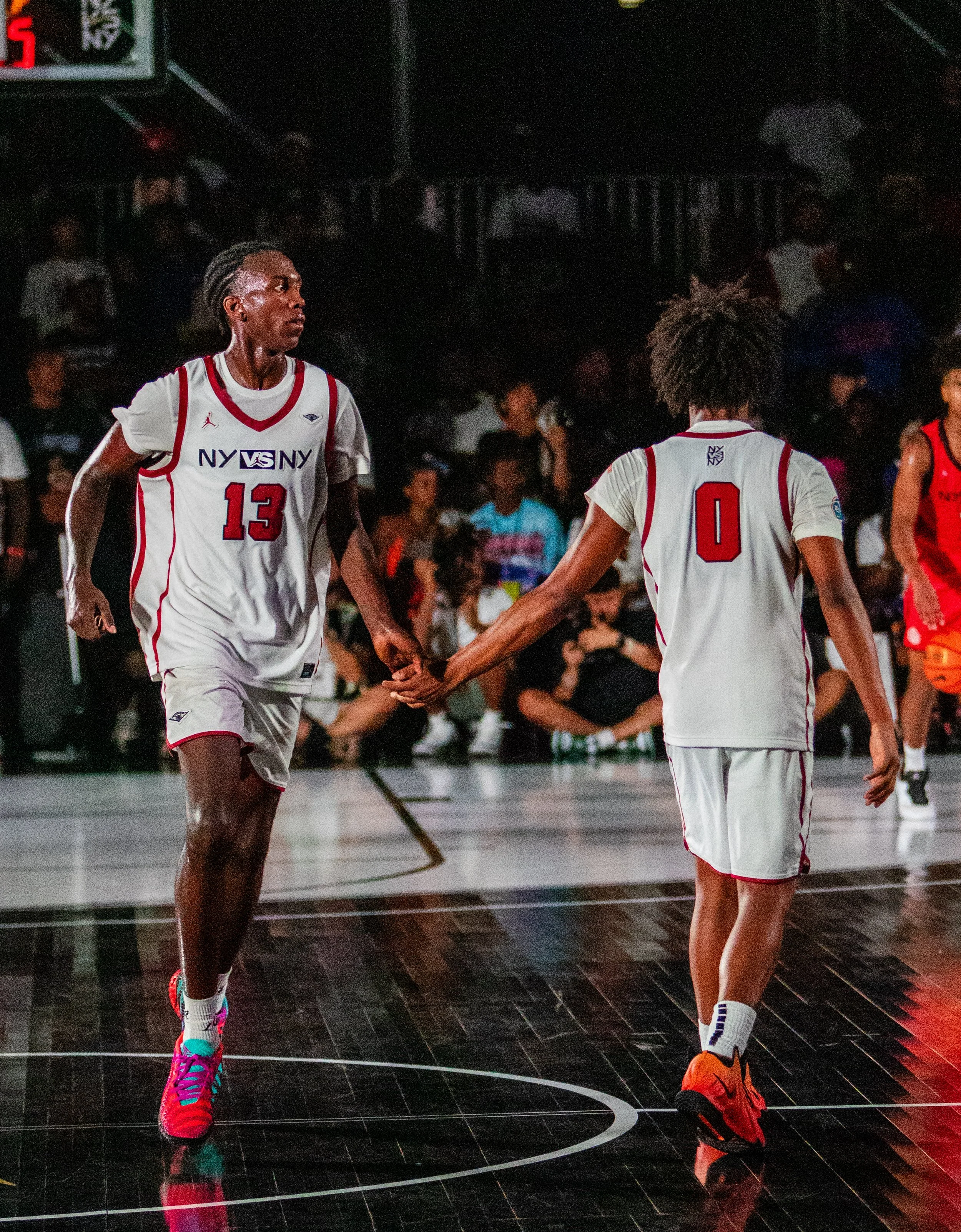 NIKE NEW YORK VS NEW YORK: VICTORY PARK CHAMPIONSHIP. Anderson Diaz, NIKE NYC, Two basketball players in white jerseys holding hands on the court during a game. Spectators are visible in the background.