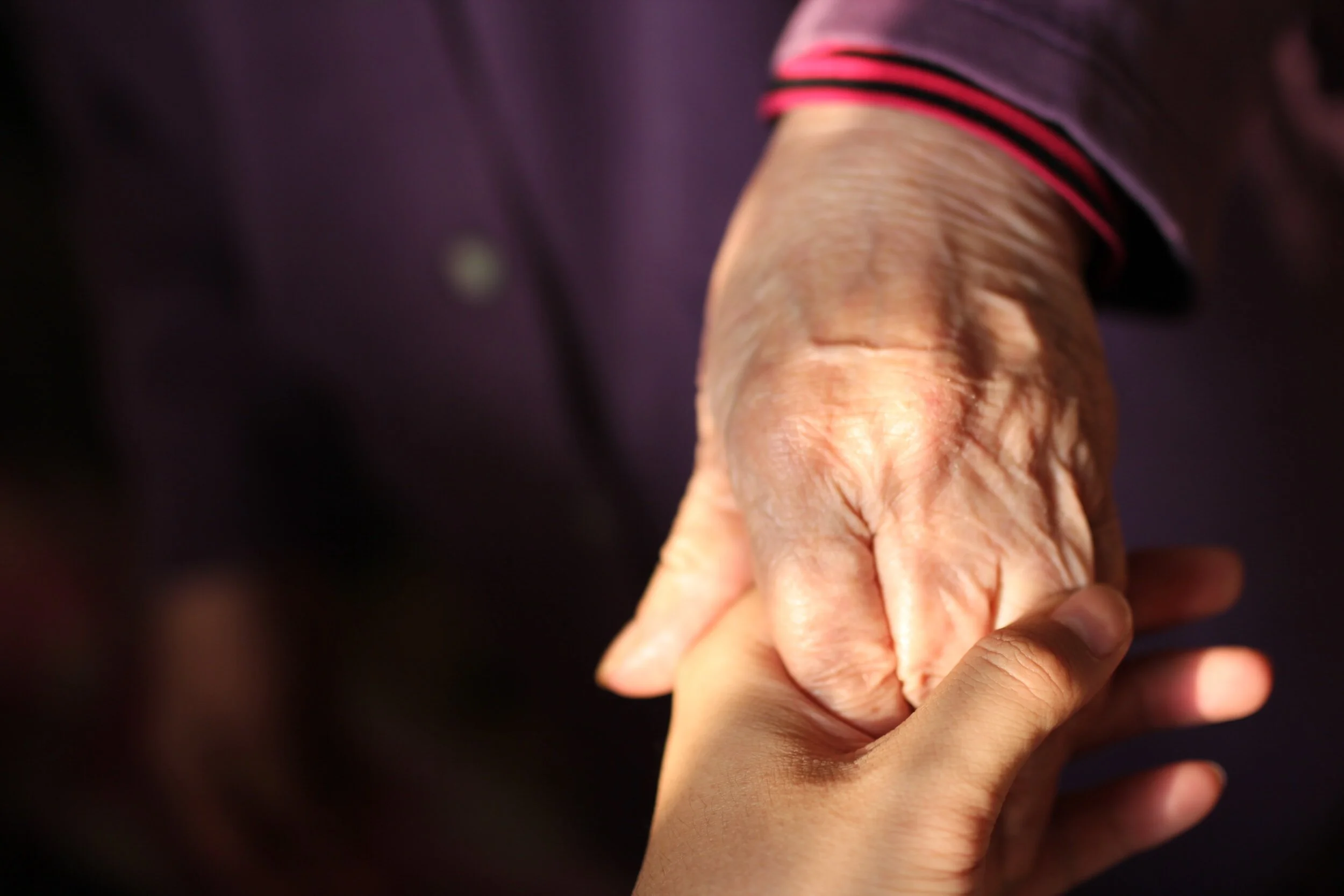 A young person's hand holding an elderly person's hand gently, symbolizing care and connection.