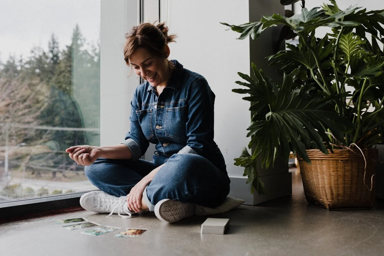 Spiritual guide sitting on floor by window smiling while looking at tarot cards in Vancouver.