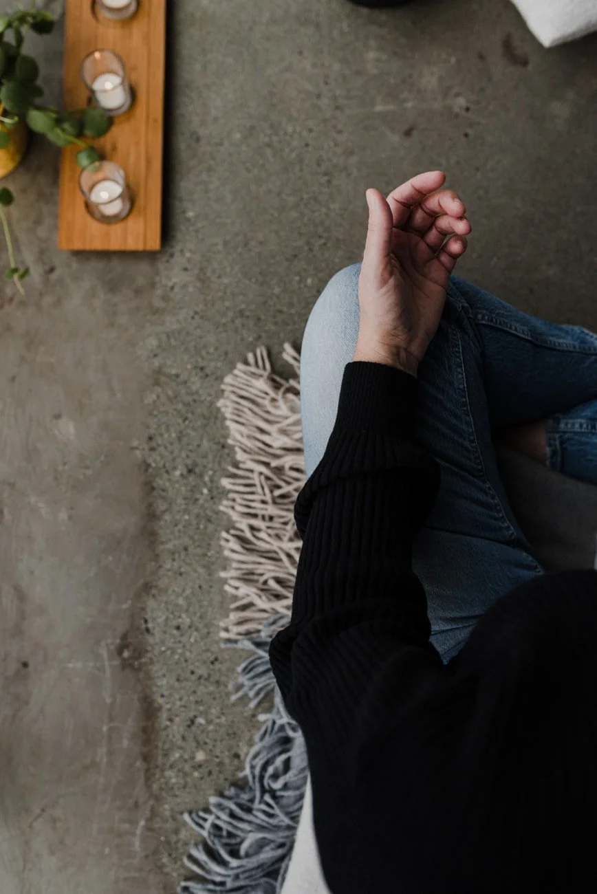Woman sitting on the ground meditation pose with candles beside her.