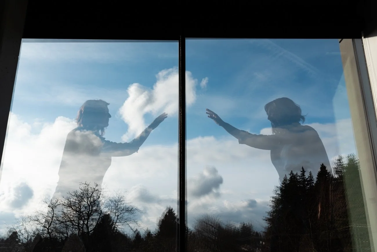 Mirror image of woman with hand reaching out to other woman. Clouds in background.