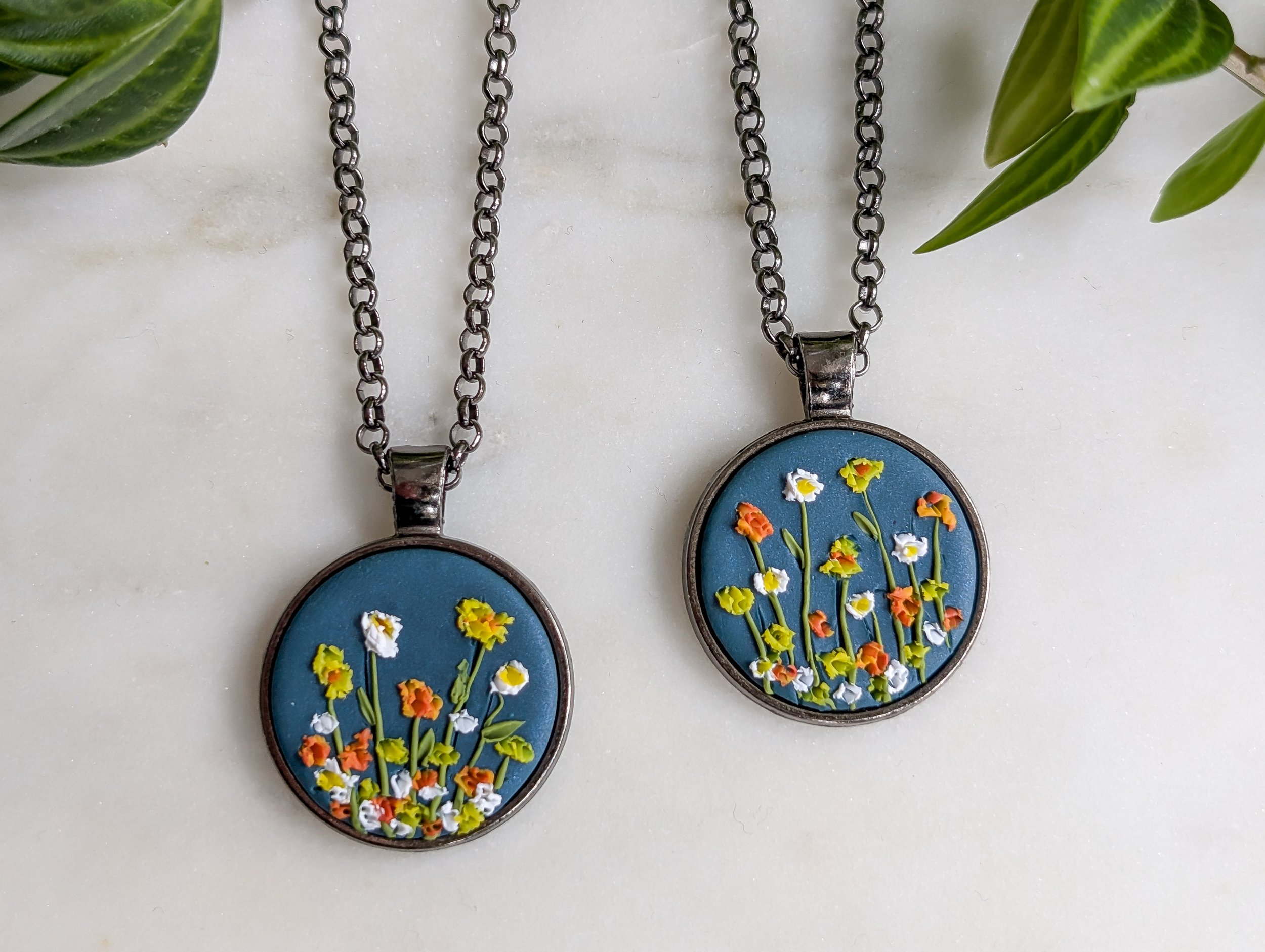 Hand sculpted wildflower pendant necklace featuring wildflowers on a navy blue background set in a gunmetal black pendant tray.