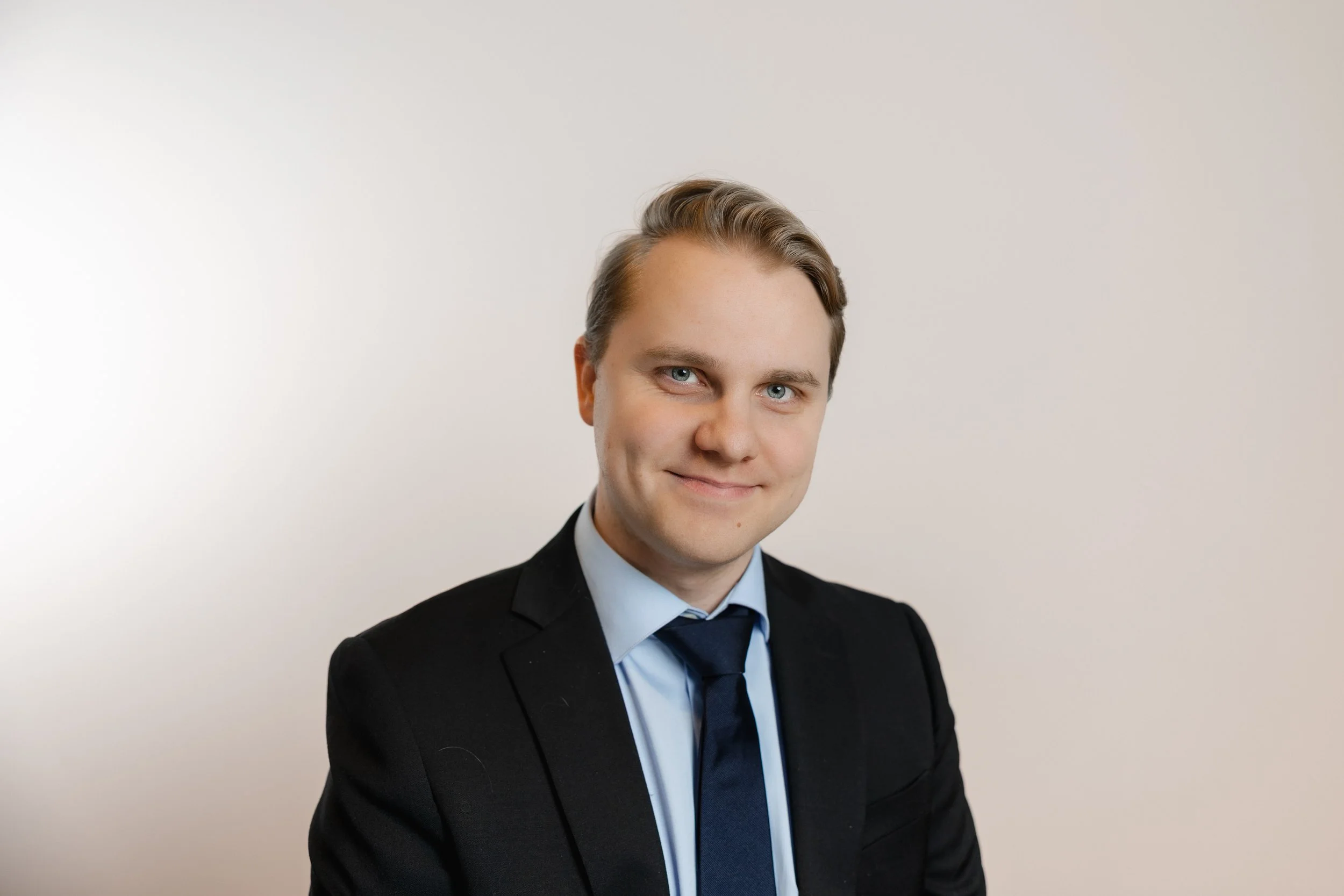 Professional portrait of a man in a suit smiling against a plain background.
