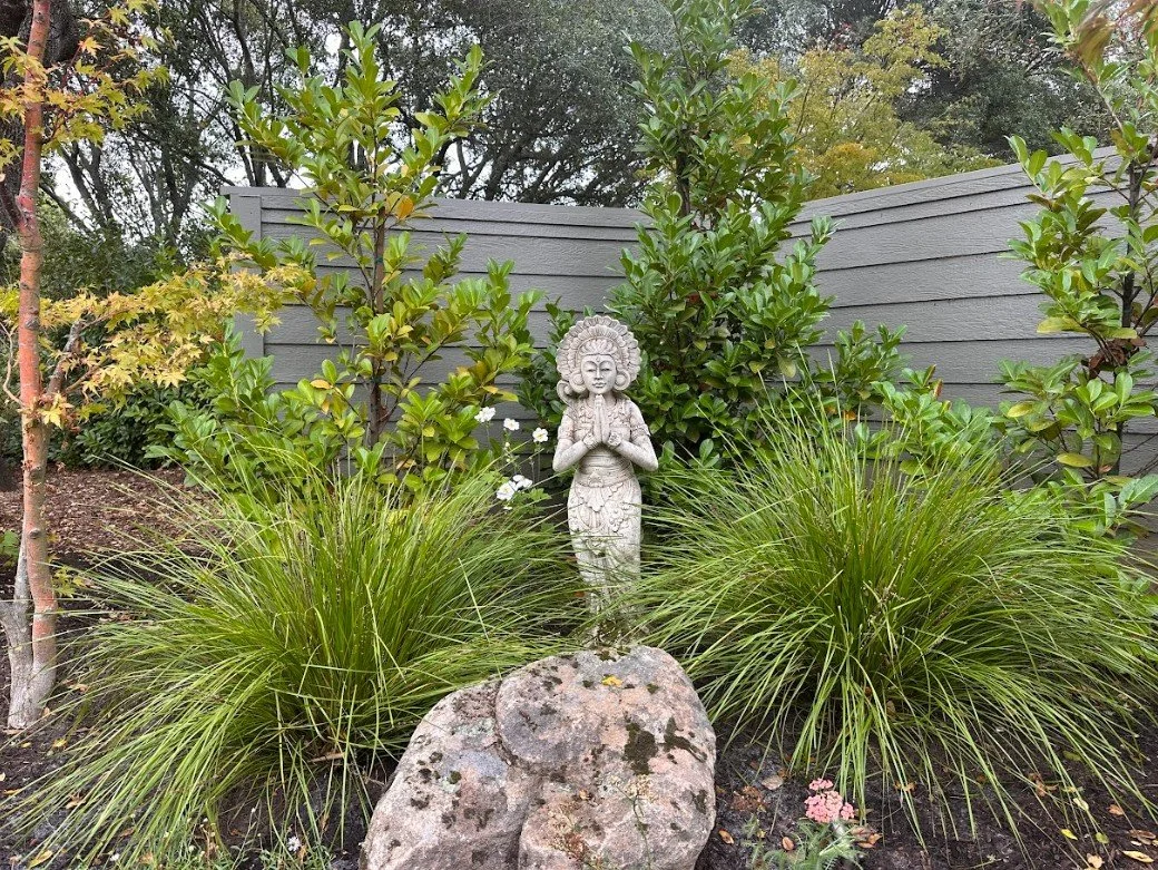 Stone statue nestled behind a Sonoma Fieldstone Boulder and Lomandra for a lush corner focal point