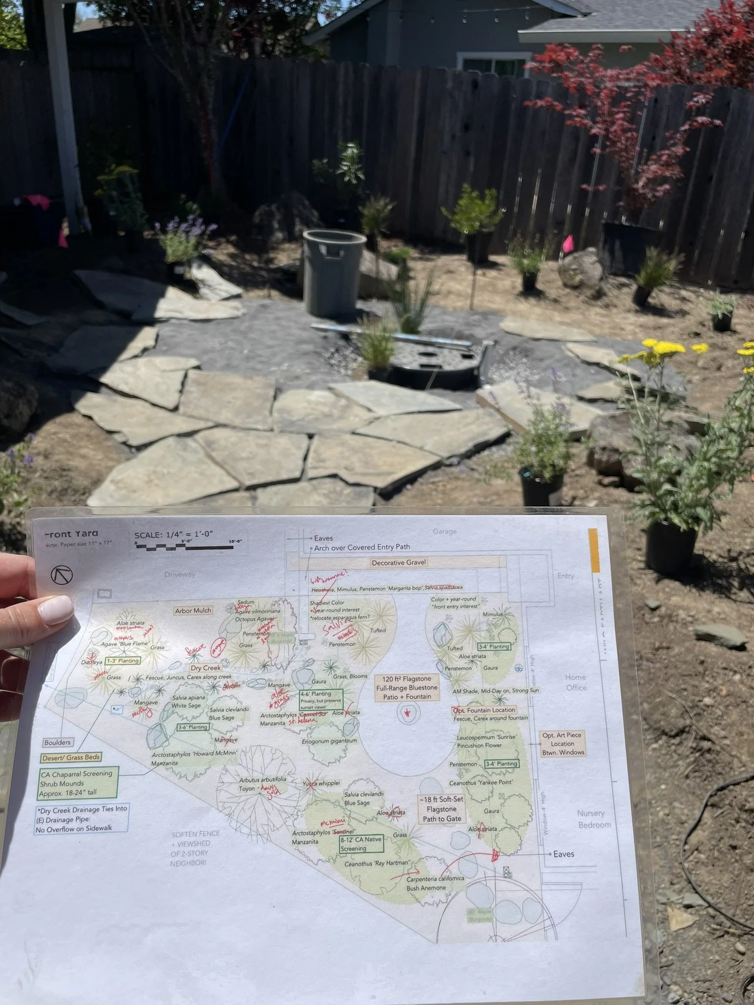 In progress shot during installation showing the printed planting plan in foreground with the boulder fountain feature and flagstone patio in the background