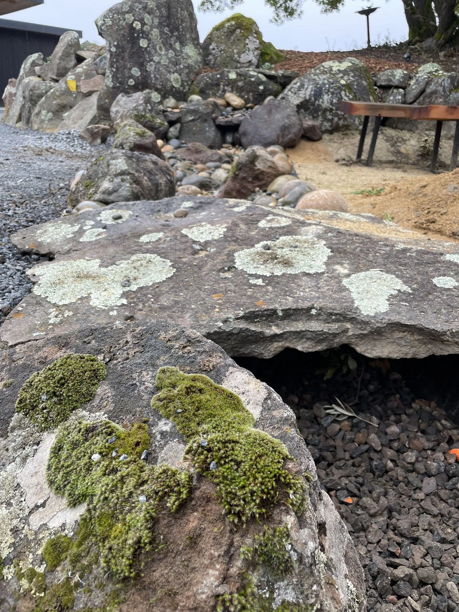 Lichen and moss covered field stone used in a dry creek bed. Large stone slab used as a bridge