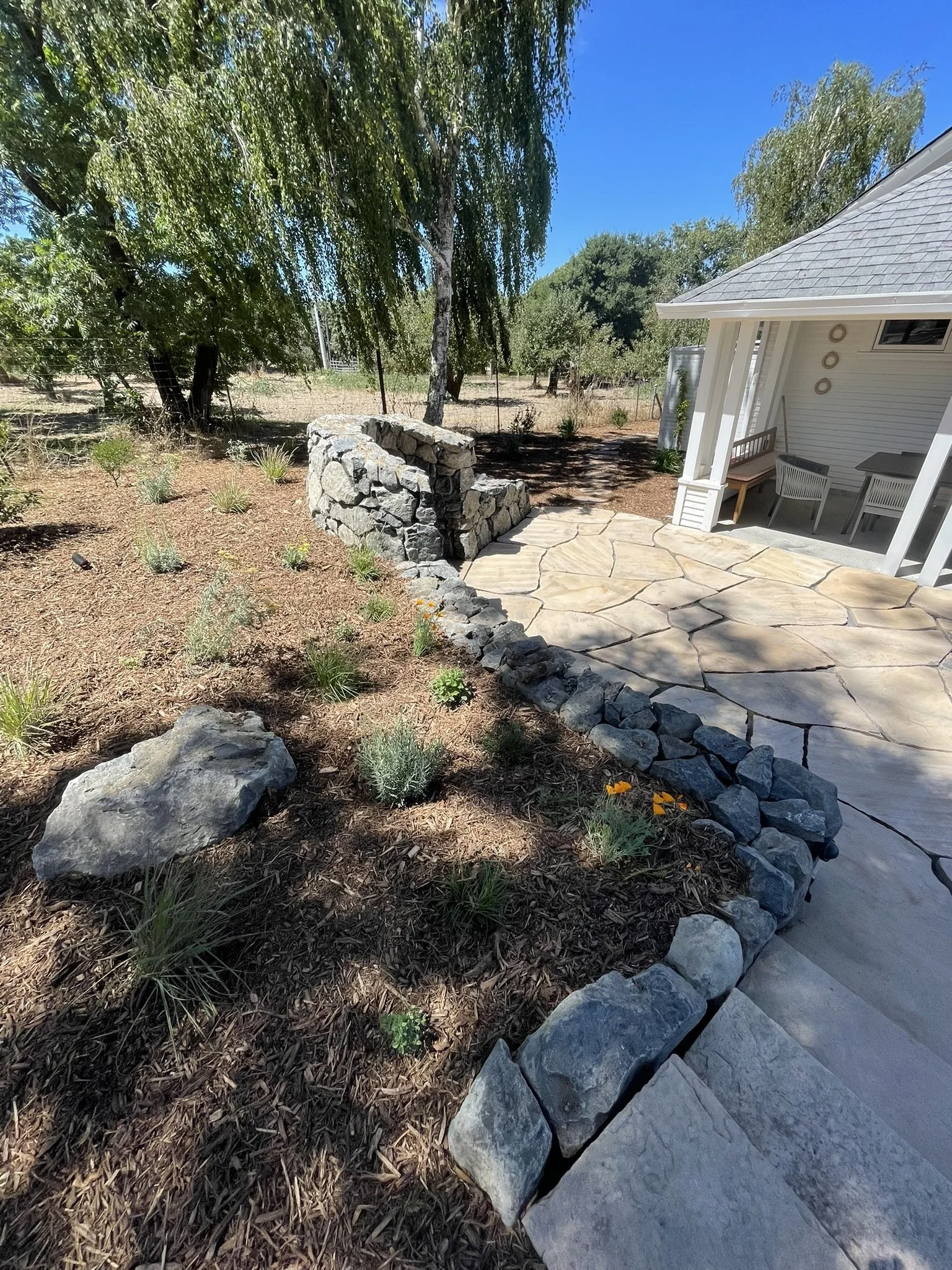 Winding retaining seat wall into stone hearth with deep planting beds above