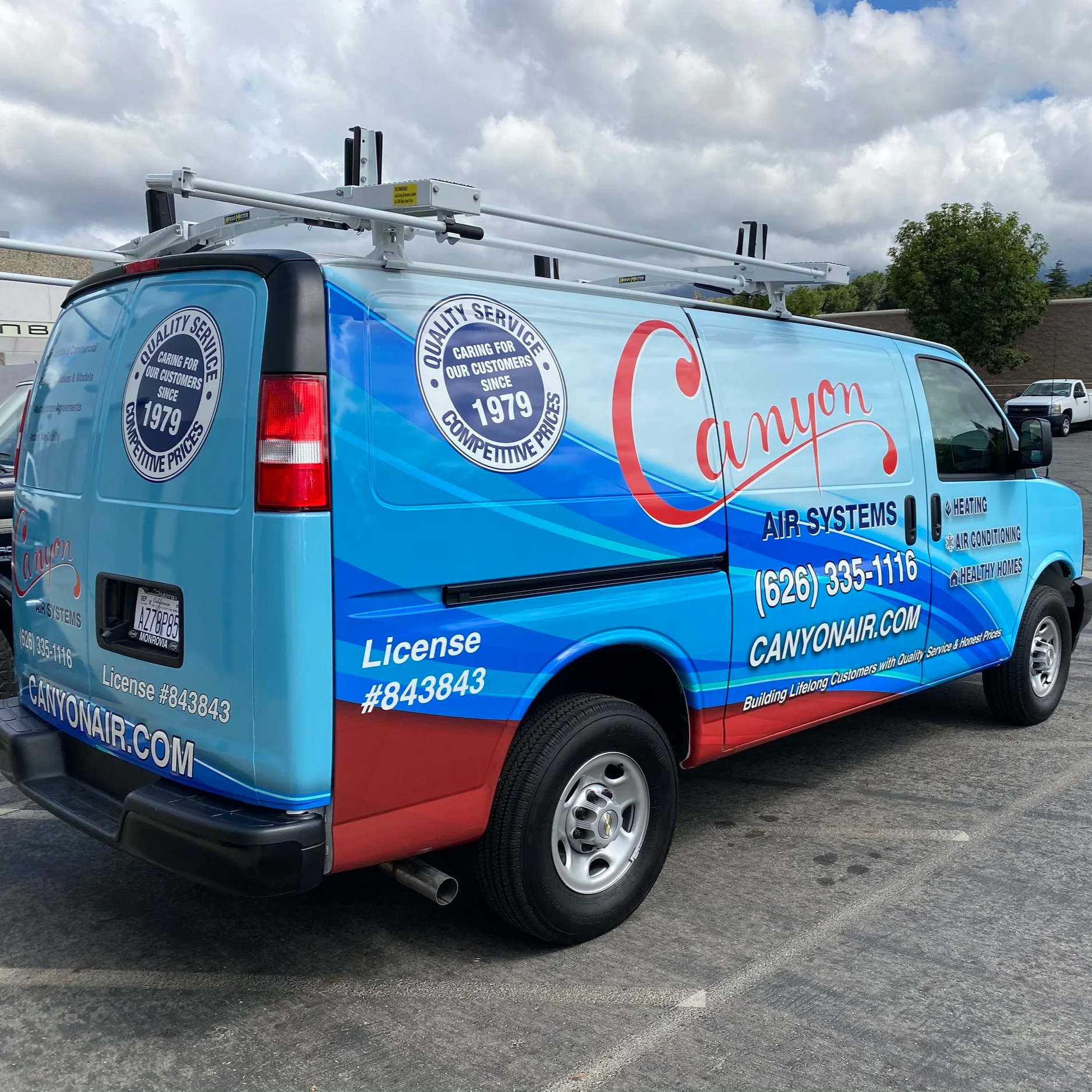 A company vehicle for Canyon Air Systems with blue, red, and white graphics, including the company name, phone number, website, and services like air conditioning, heating, and healthy home solutions. The van has ladder racks on top.