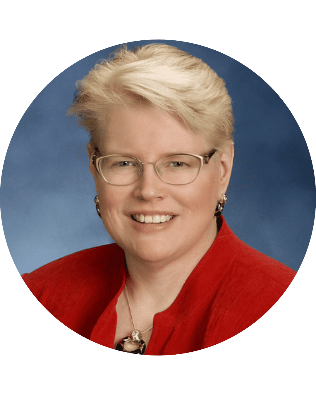 A woman with short blonde hair, glasses, and earrings, wearing a red blazer, smiling at the camera.