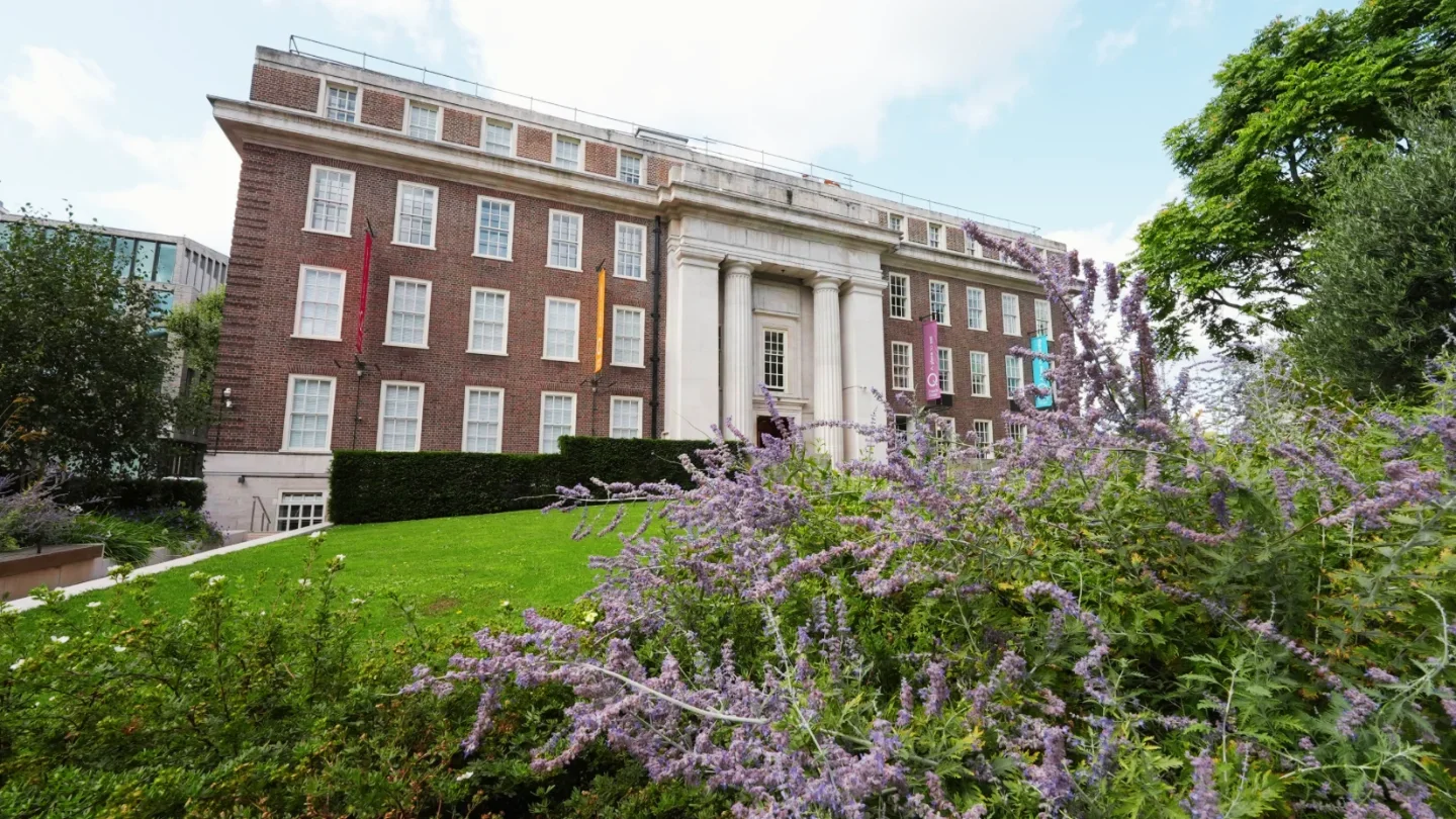 Recovery Reimagined London 2024 conference venue with a red brick building, green lawn, and purple flowers.
