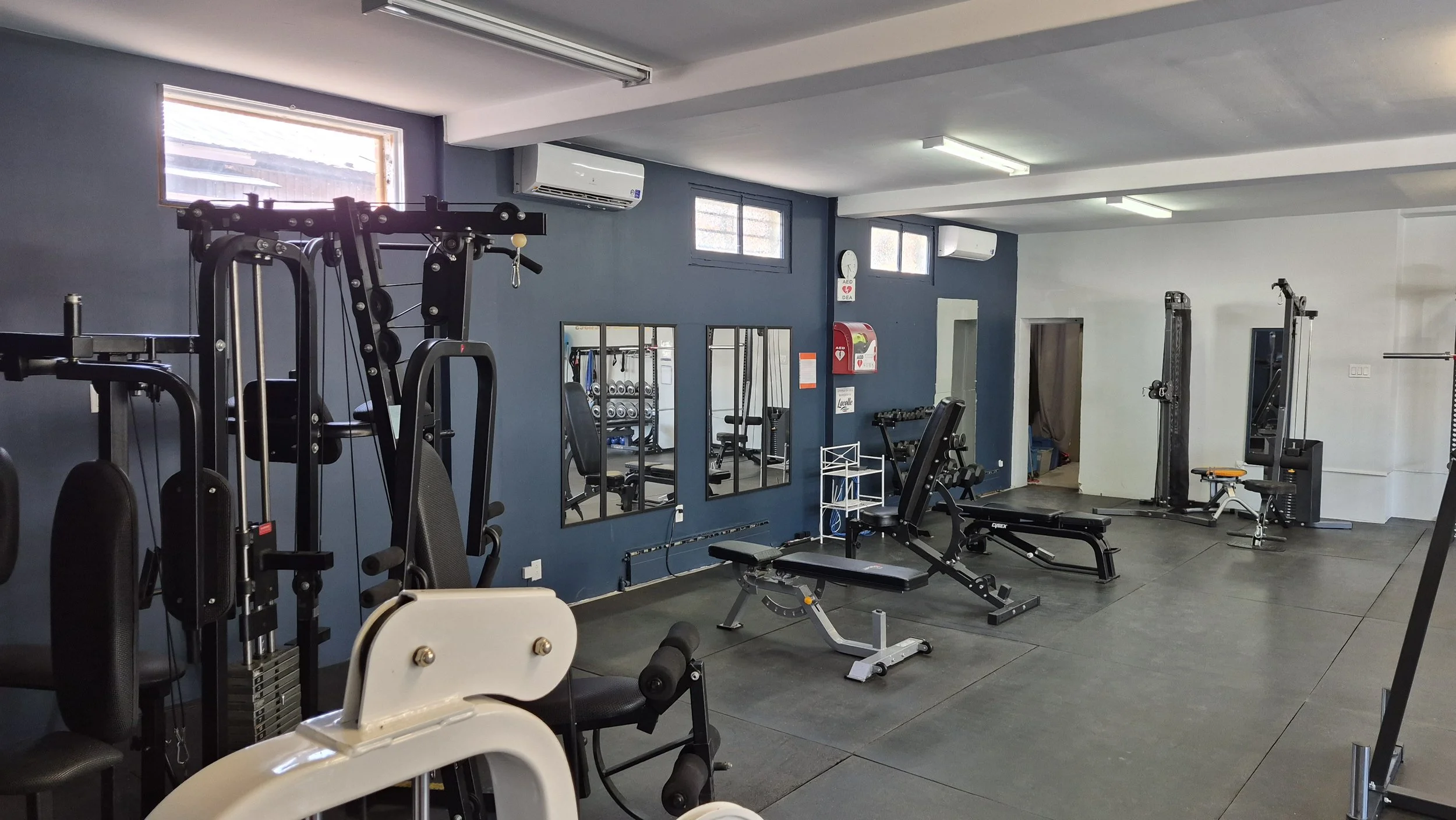 Appareilles de musculations dans un décor lumineux, un mur bleu foncé avec des miroirs et un appareil défibrillateur