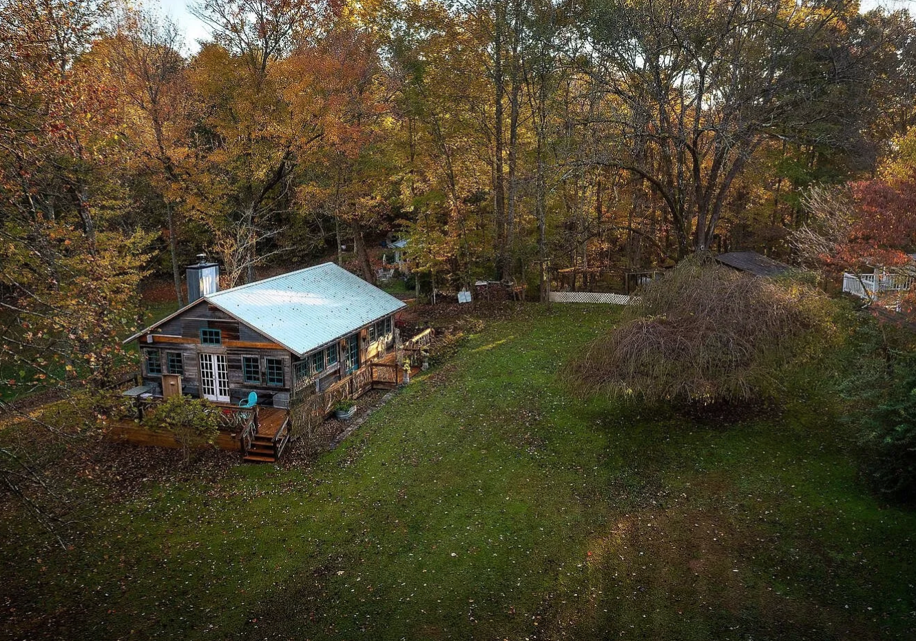 A photo of Stoneroot Retreat in autumn. A building sits in a large grassy area, surrounded by a lush forest