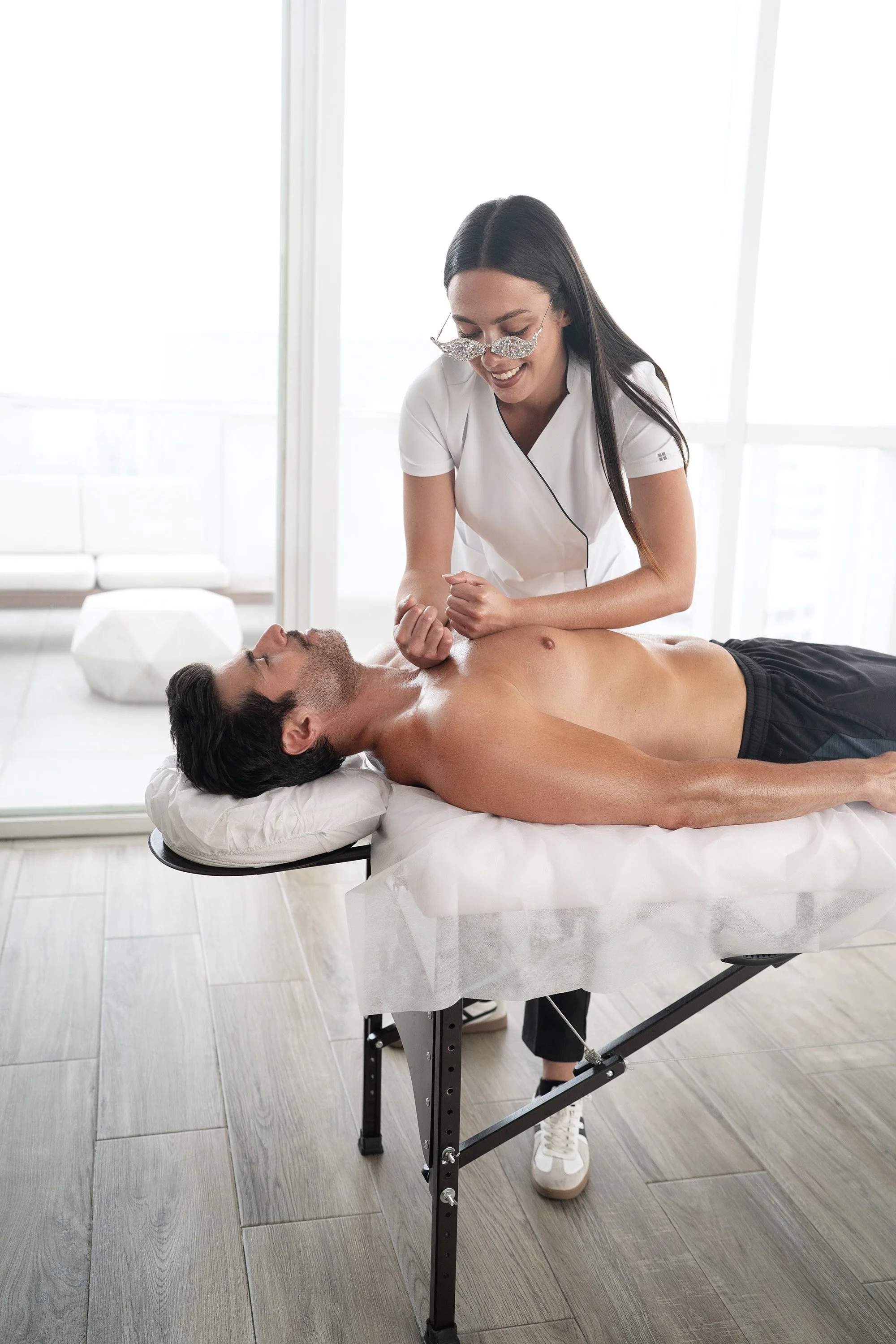 Terapeuta aplicando presión profunda en pecho y hombros de un cliente recostado en camilla dentro de un estudio luminoso.