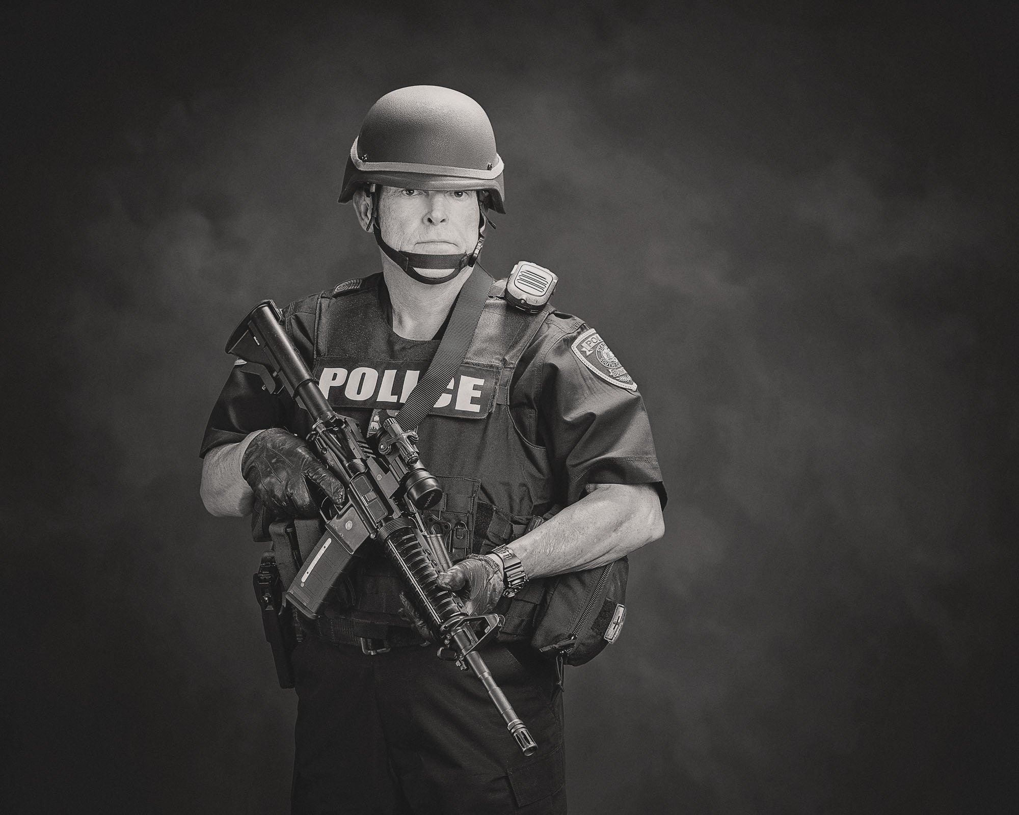 Black and white portrait of a SWAT officer in helmet and tactical vest holding his rifle