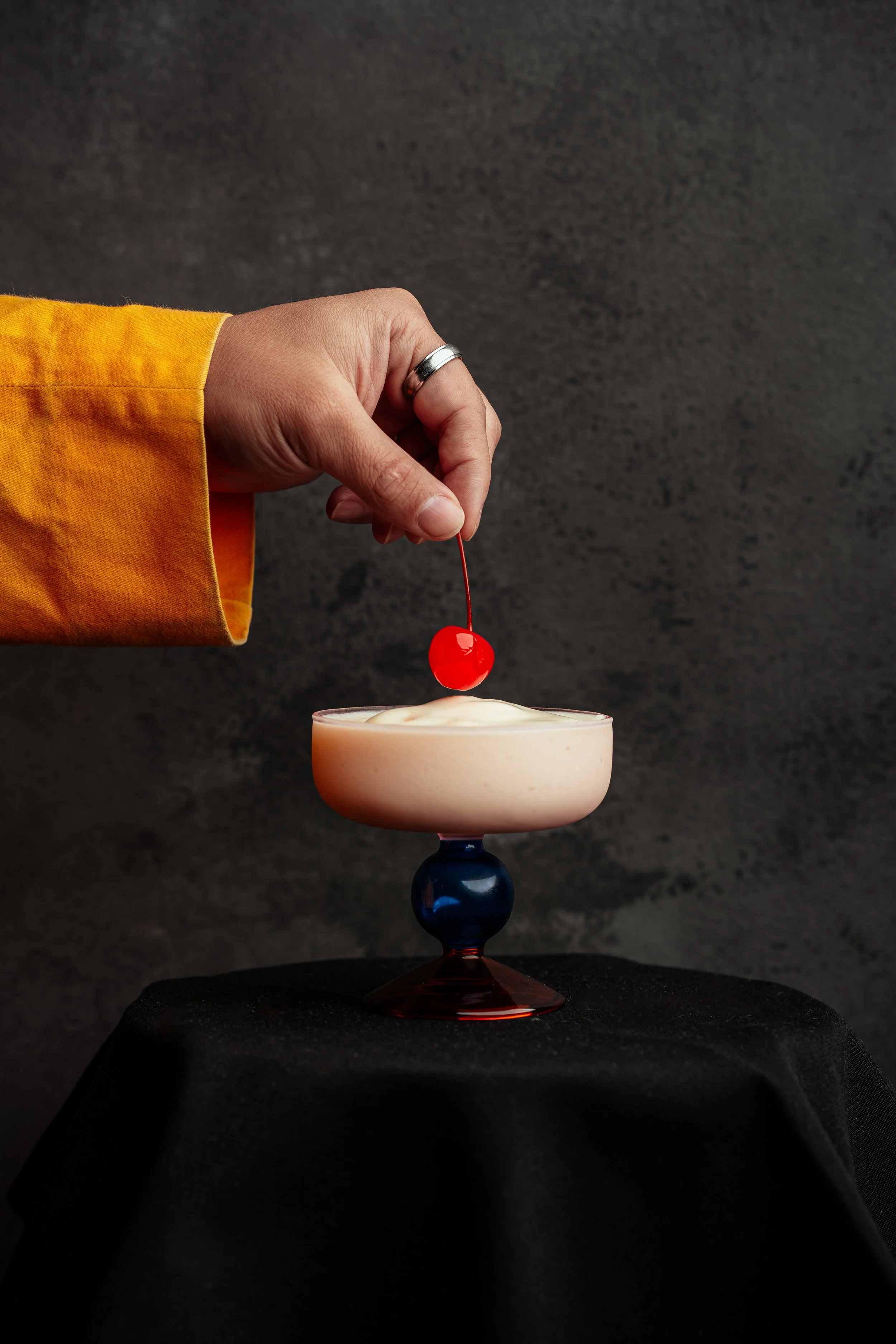 Person wearing a yellow sleeve adding a cherry on top of a dessert in a glass bowl.