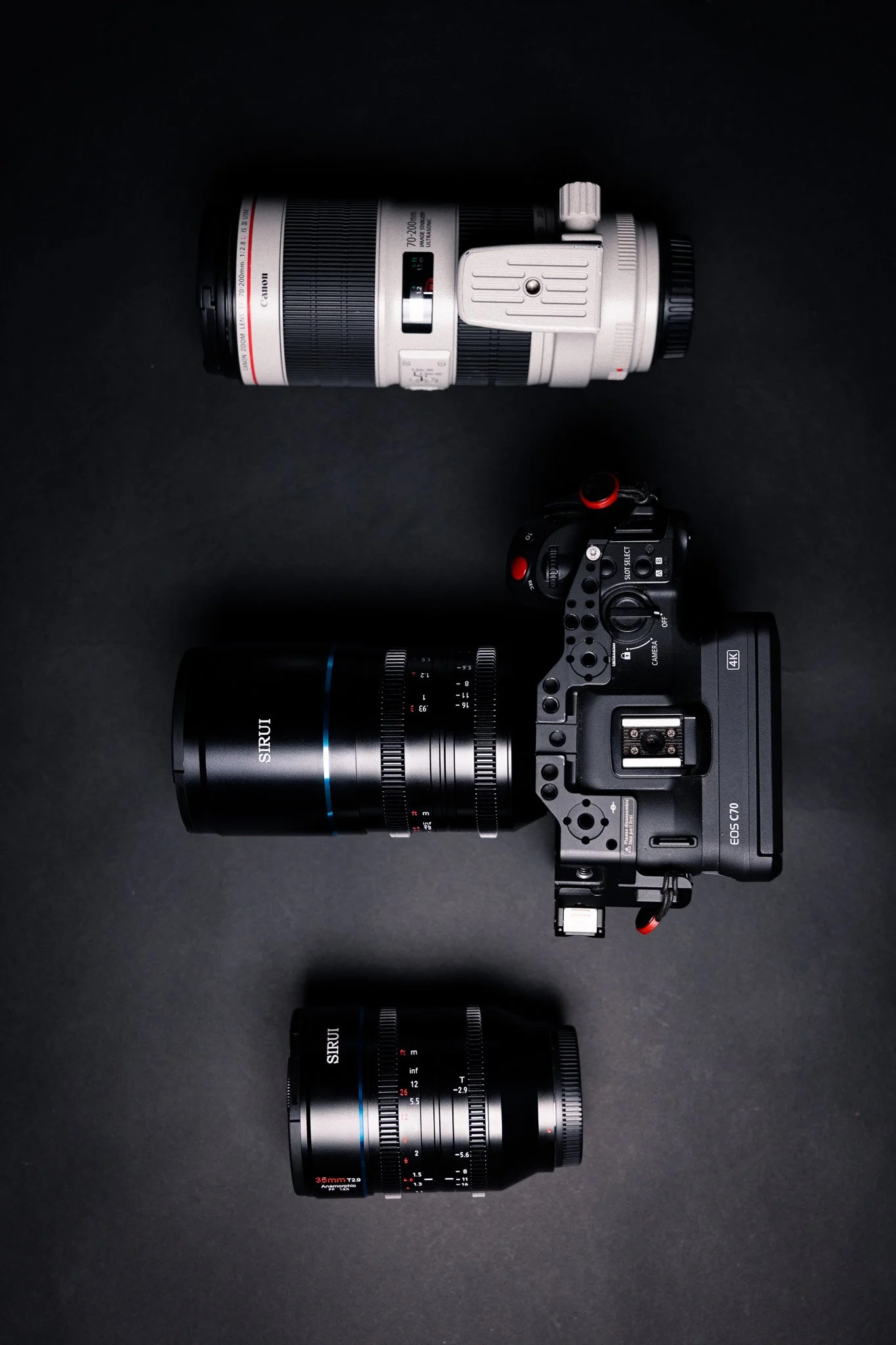 Image shows a professional camera with a large lens on a black background, accompanied by a telephoto lens and a camera control or accessory.