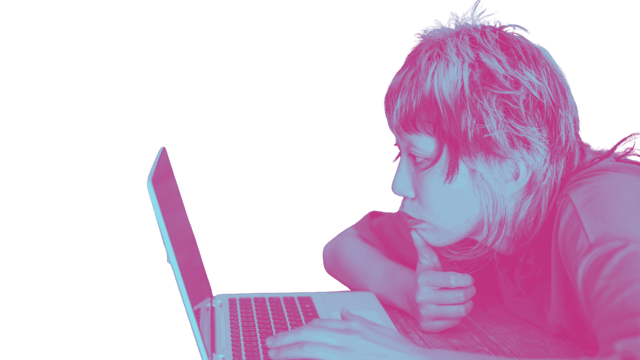 A person with shoulder-length hair looking intently at a laptop screen, resting their chin on their hand.