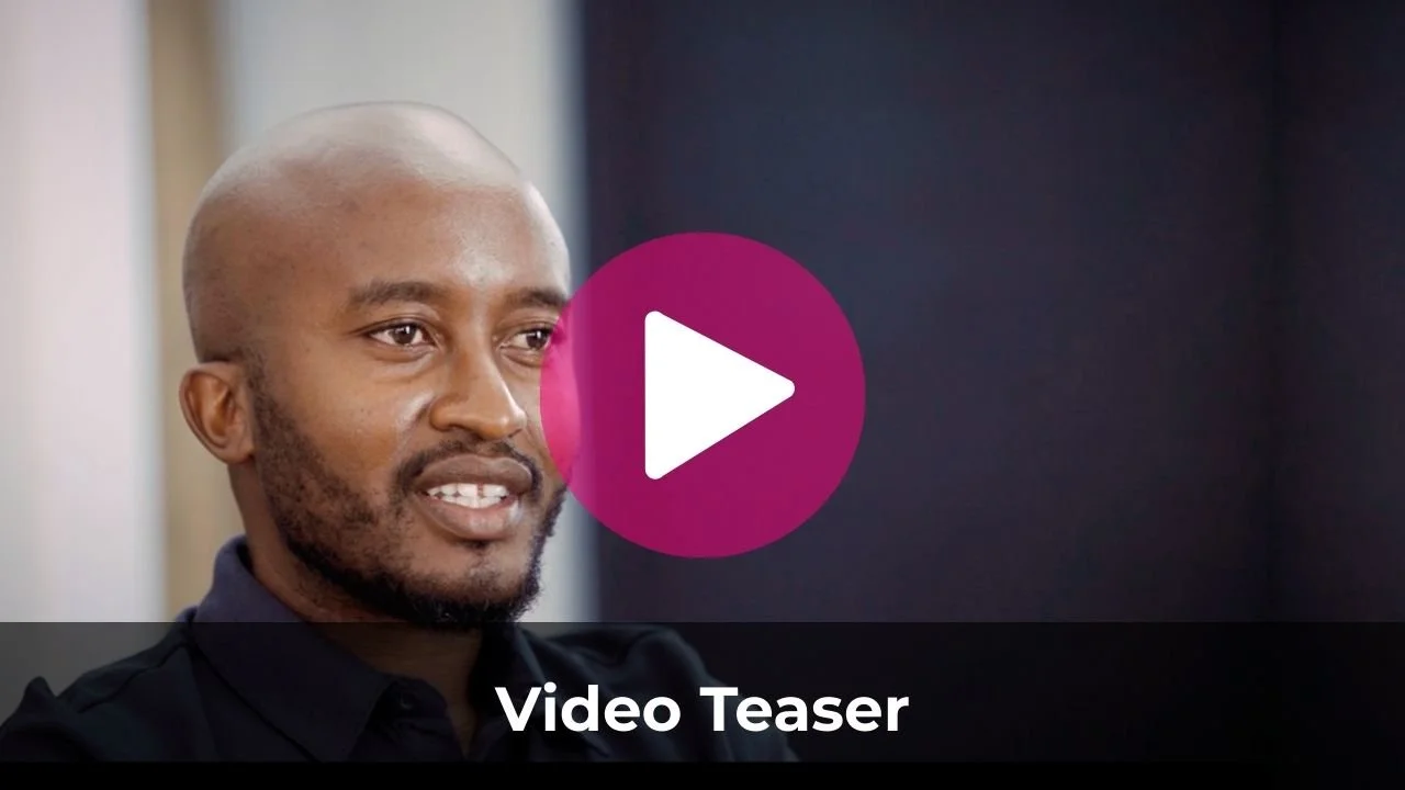 A man with a shaved head and beard, wearing a dark shirt, speaking in an interview or video setting.