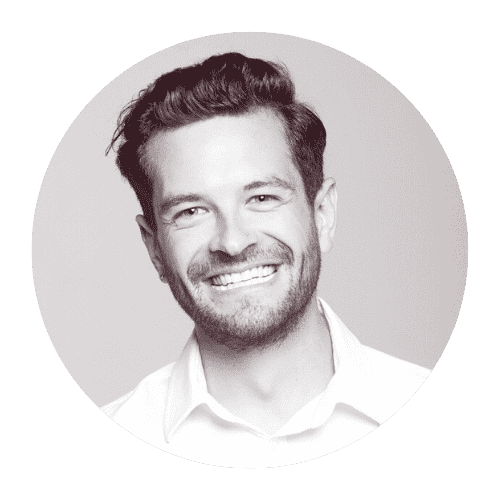 Black-and-white portrait of a smiling man with short, styled hair and a beard, wearing a collared shirt.