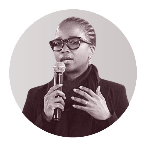 Woman with glasses and earrings speaking into a microphone