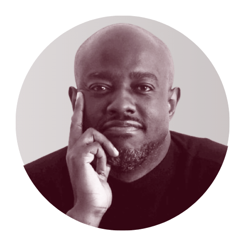 A black man with a bald head and beard, resting his chin on his hand, looking thoughtful.