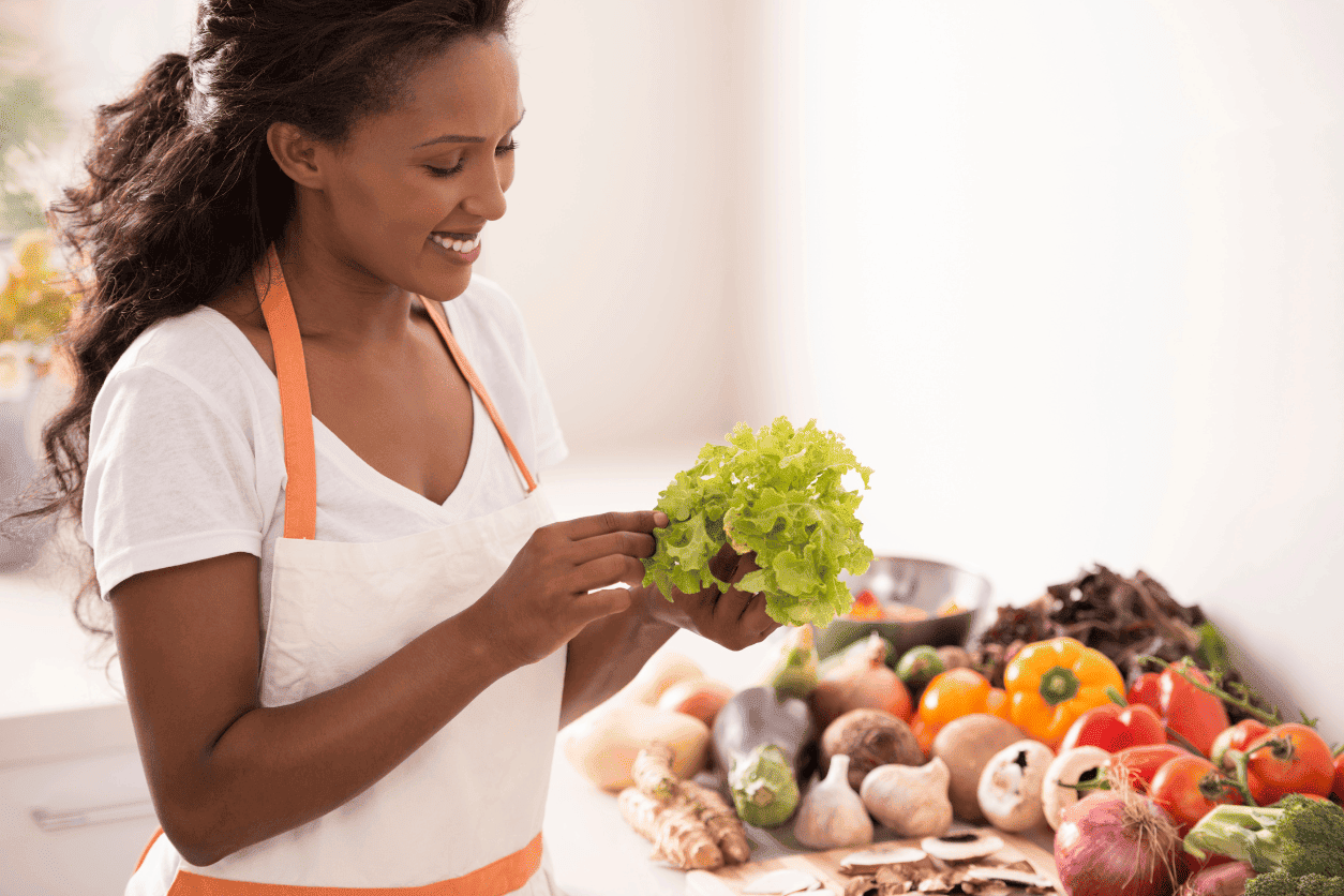 Woman in apron holding lettuce with assorted vegetables on table