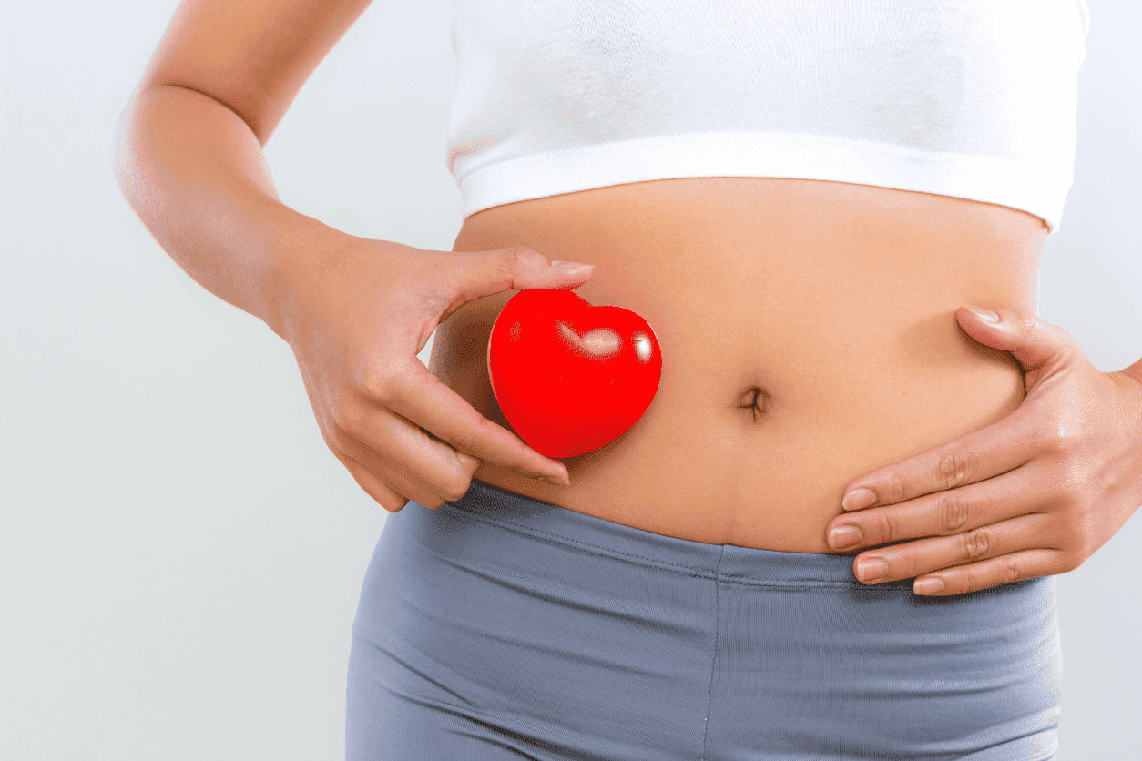 Woman holding a red heart shape on her stomach, implying health or love.