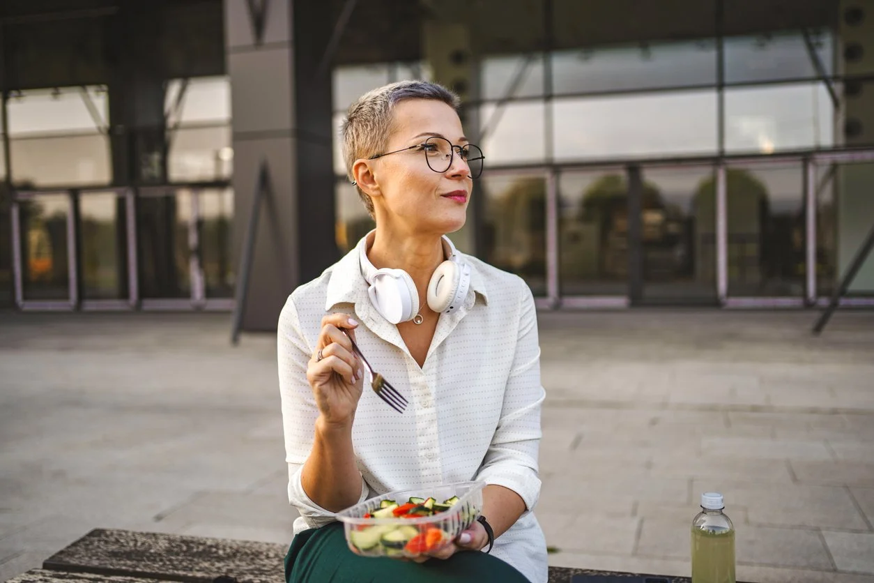 A woman wearing headphones while holding a bowl of salad