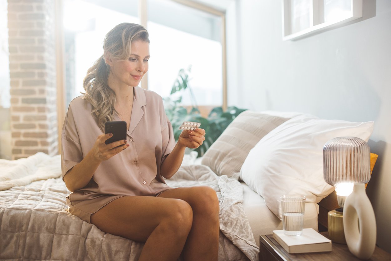 Perimenopausal woman sitting on bed, holding medicine