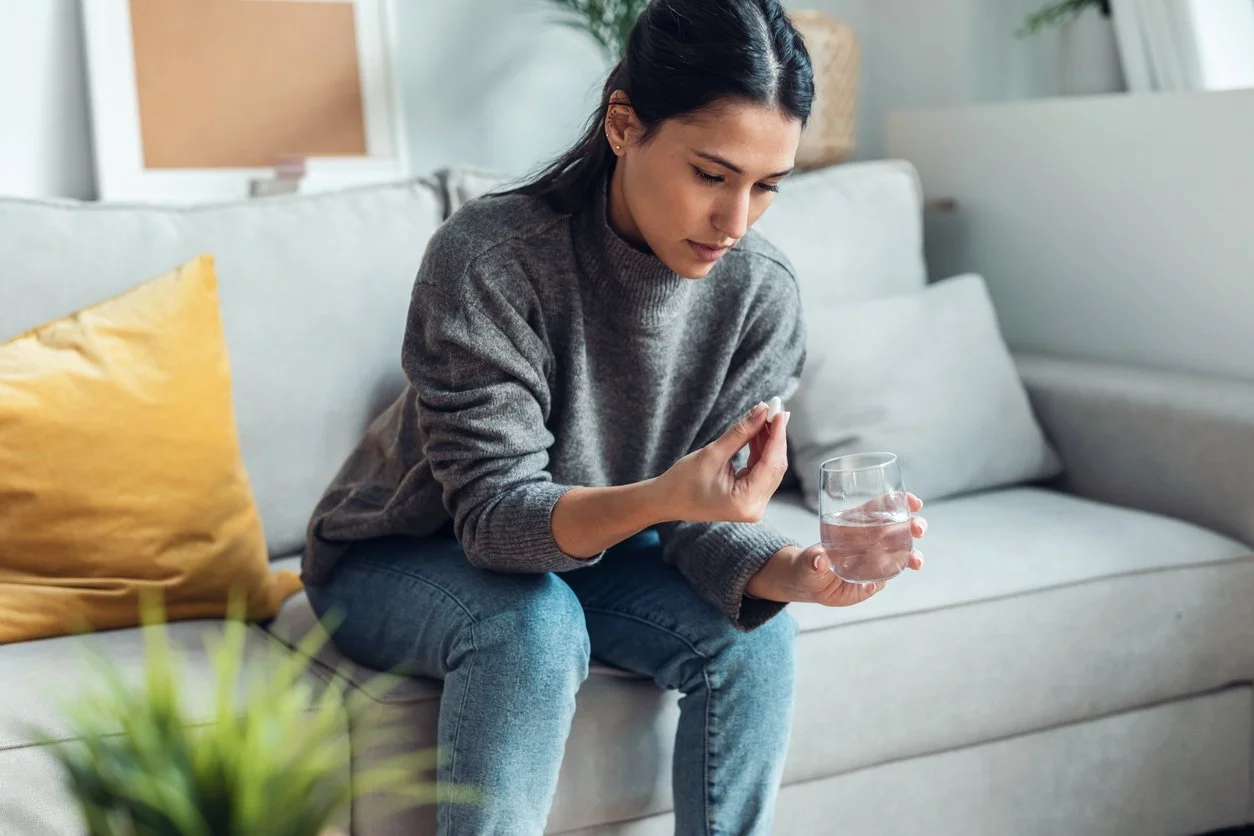 Woman sitting on couch holding a glass of water & medicine
