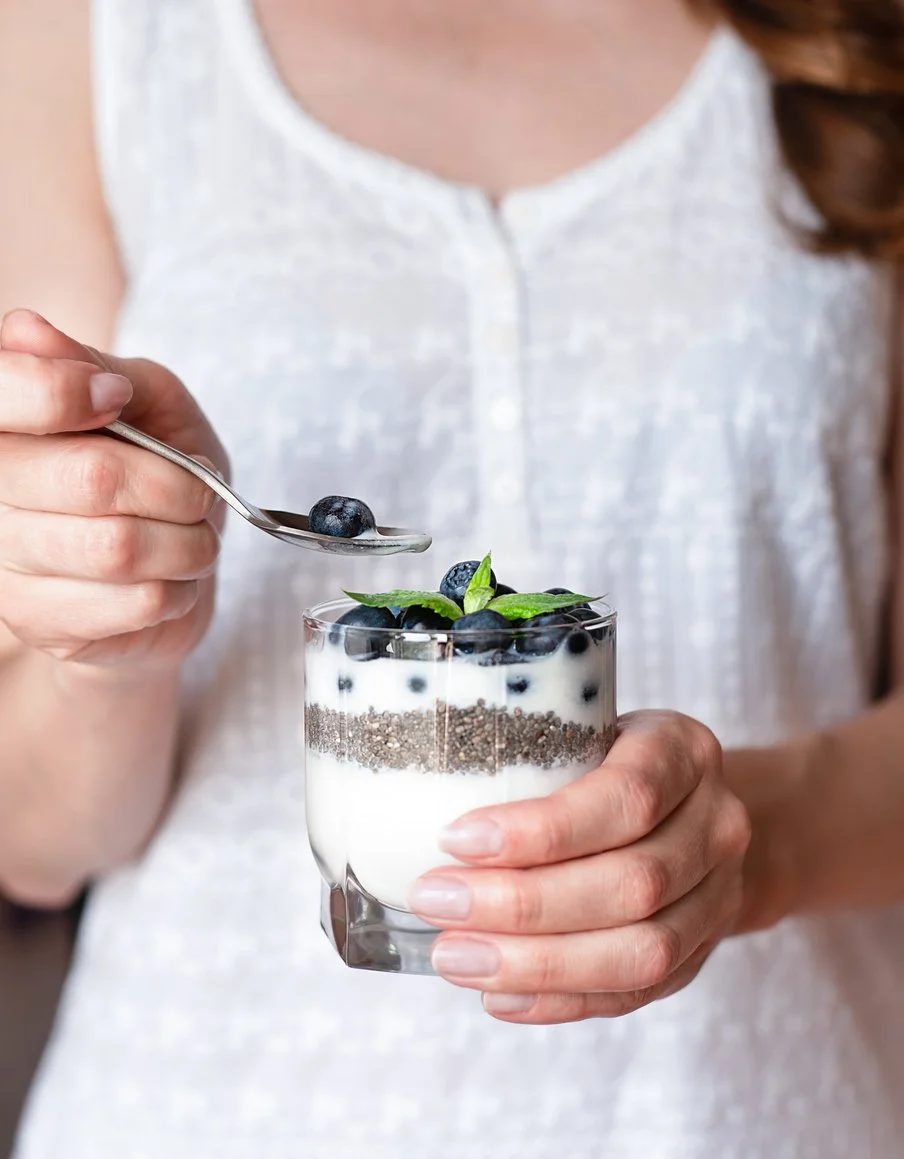 A close-up photo of a woman holding a yogurt parfait with berries and chia seeds