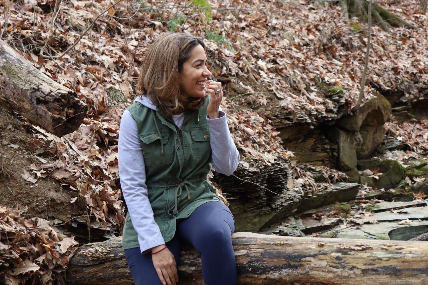 Dr. Sarah Bonza sitting on a log in a forest during autumn