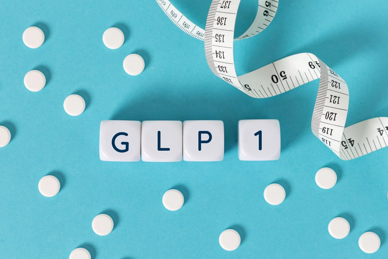 GLP 1 word on blocks surrounded by medicine pills and measuring tape on blue background